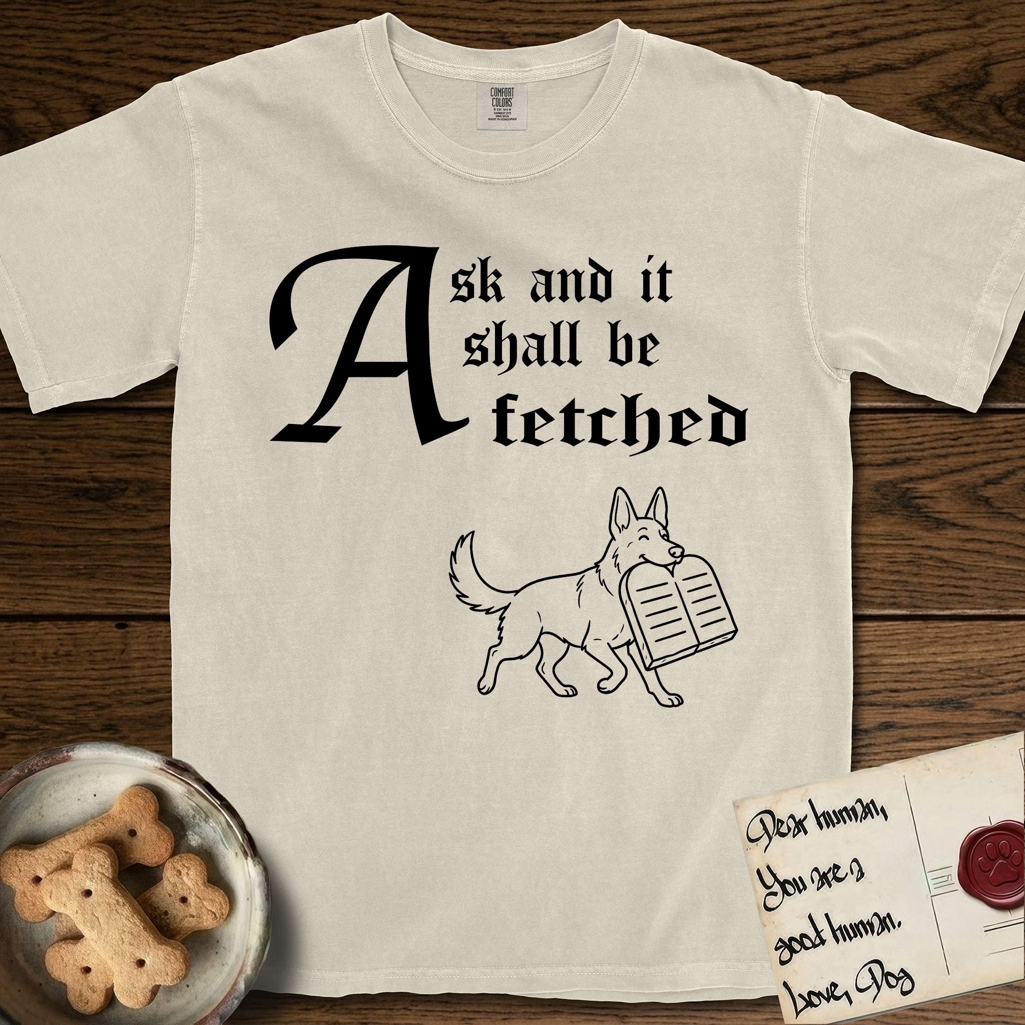 Ask and It Shall Be Fetched German Shepherd T-Shirt flat lay in Ivory, featuring a sparse pen-and-ink illustration of a German Shepherd at a proud trot carrying a pair of stone tablets.