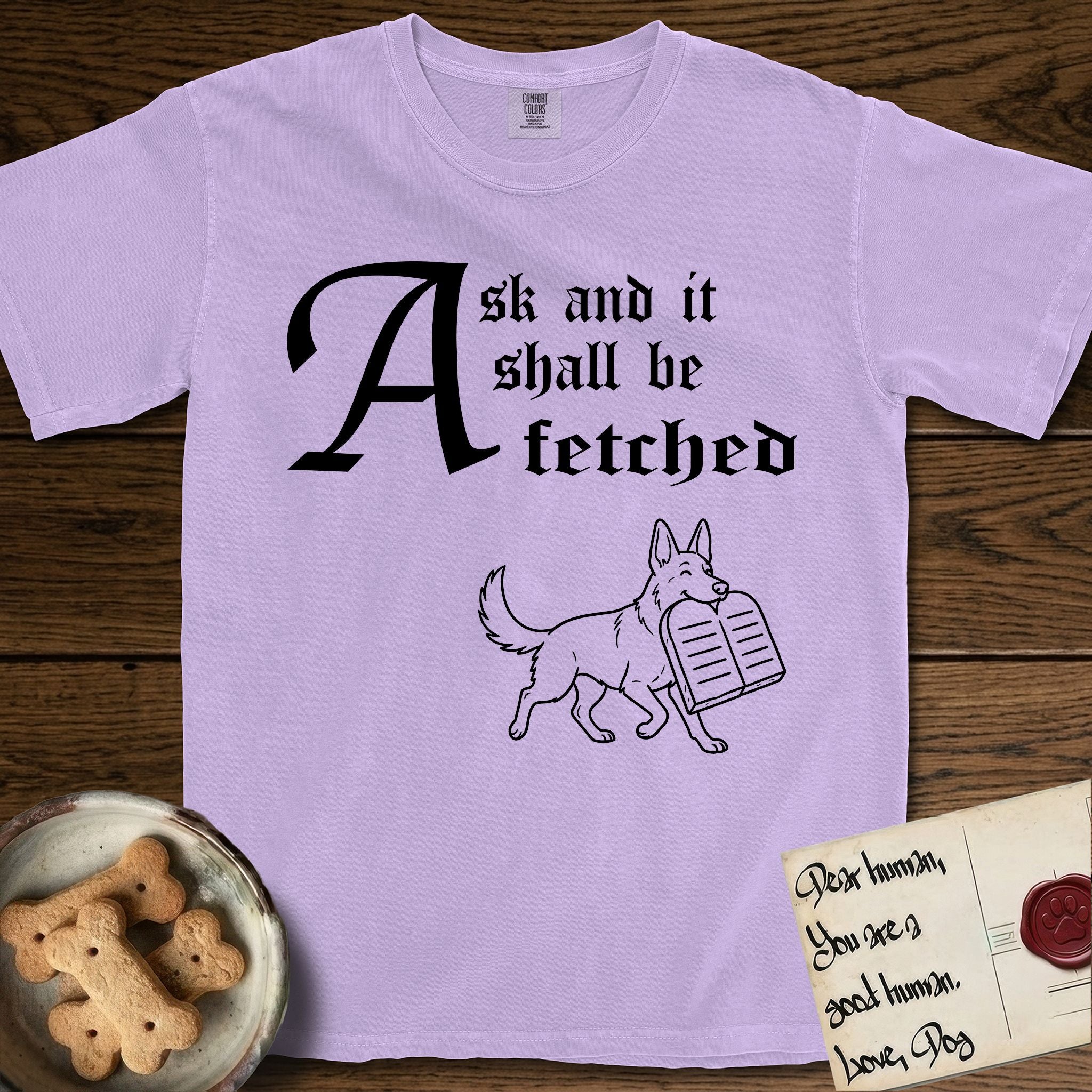 Ask and It Shall Be Fetched German Shepherd T-Shirt flat lay in Orchid, featuring a sparse pen-and-ink illustration of a German Shepherd at a proud trot carrying a pair of stone tablets.