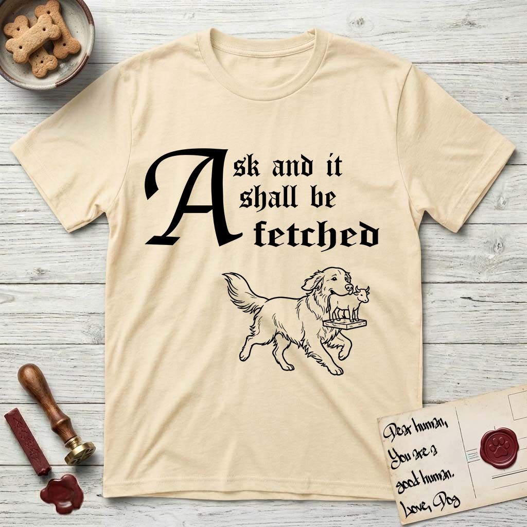 Ask and It Shall Be Fetched Golden Retriever T-Shirt flat lay in Natural, featuring a sparse pen-and-ink illustration of a Golden Retriever at a proud trot carrying a golden calf idol on a plinth.