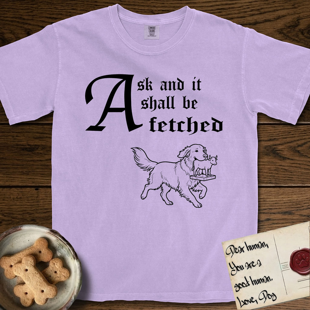 Ask and It Shall Be Fetched Golden Retriever T-Shirt flat lay in Orchid, featuring a sparse pen-and-ink illustration of a Golden Retriever at a proud trot carrying a golden calf idol on a plinth.