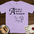 Ask and It Shall Be Fetched Golden Retriever T-Shirt flat lay in Orchid, featuring a sparse pen-and-ink illustration of a Golden Retriever at a proud trot carrying a golden calf idol on a plinth.