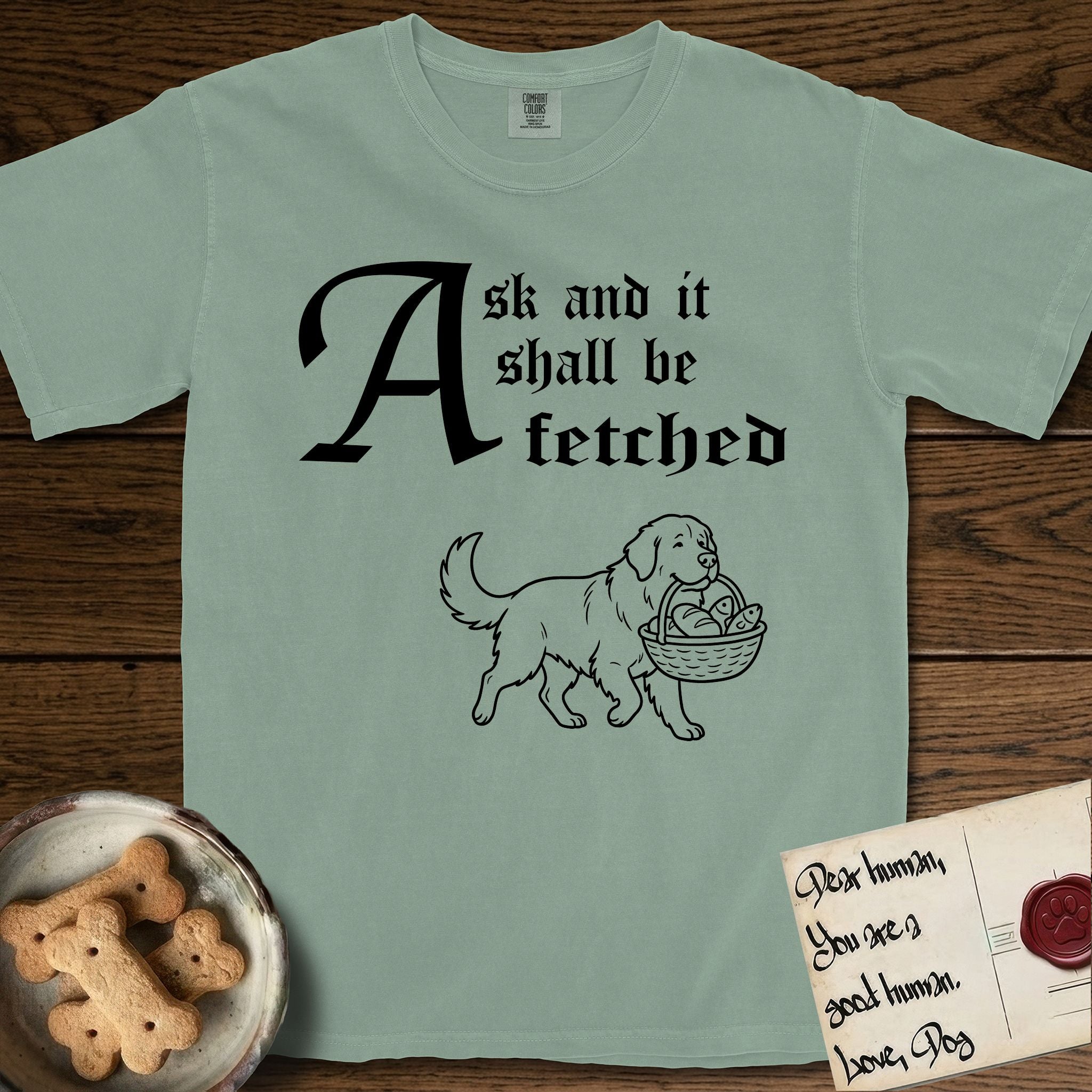 Ask and It Shall Be Fetched Newfoundland T-Shirt flat lay in Bay, featuring a sparse pen-and-ink illustration of a Newfoundland at a proud trot carrying loaves and fishes.