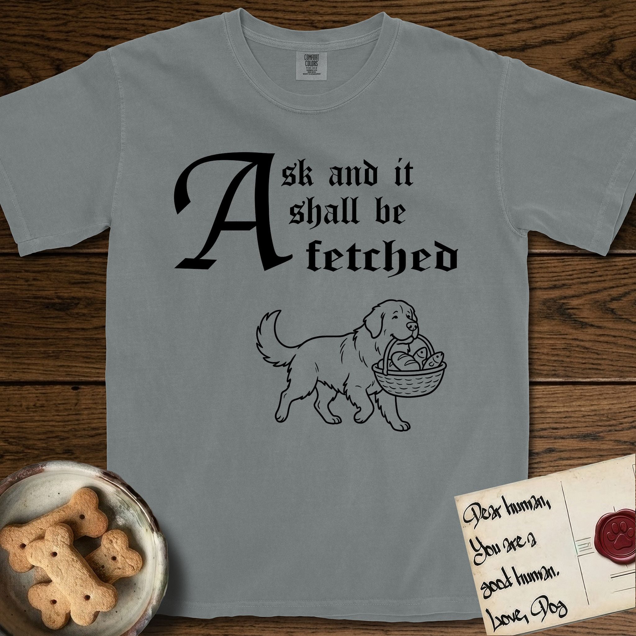 Ask and It Shall Be Fetched Newfoundland T-Shirt flat lay in Granite, featuring a sparse pen-and-ink illustration of a Newfoundland at a proud trot carrying loaves and fishes.
