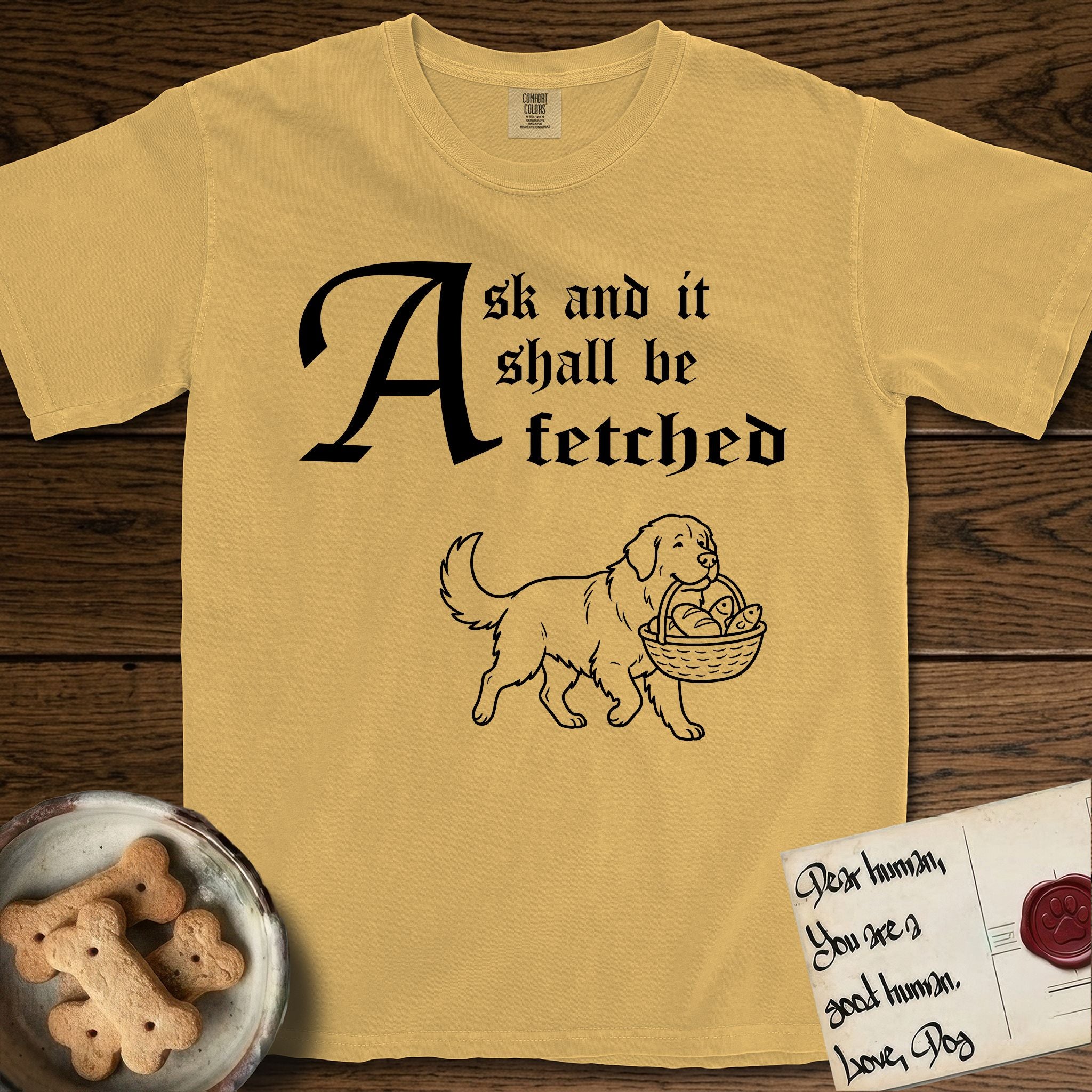 Ask and It Shall Be Fetched Newfoundland T-Shirt flat lay in Mustard, featuring a sparse pen-and-ink illustration of a Newfoundland at a proud trot carrying loaves and fishes.