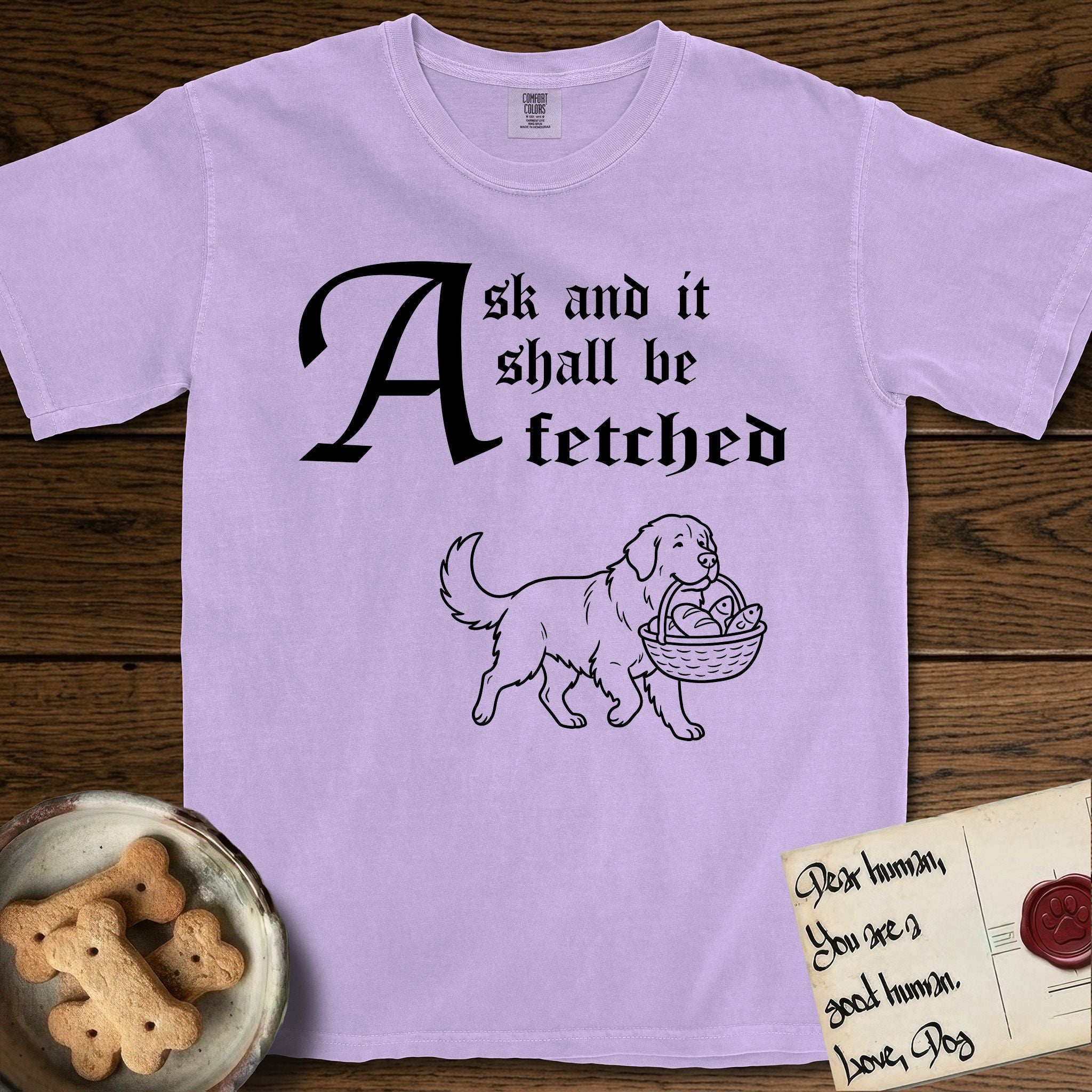Ask and It Shall Be Fetched Newfoundland T-Shirt flat lay in Orchid, featuring a sparse pen-and-ink illustration of a Newfoundland at a proud trot carrying loaves and fishes.