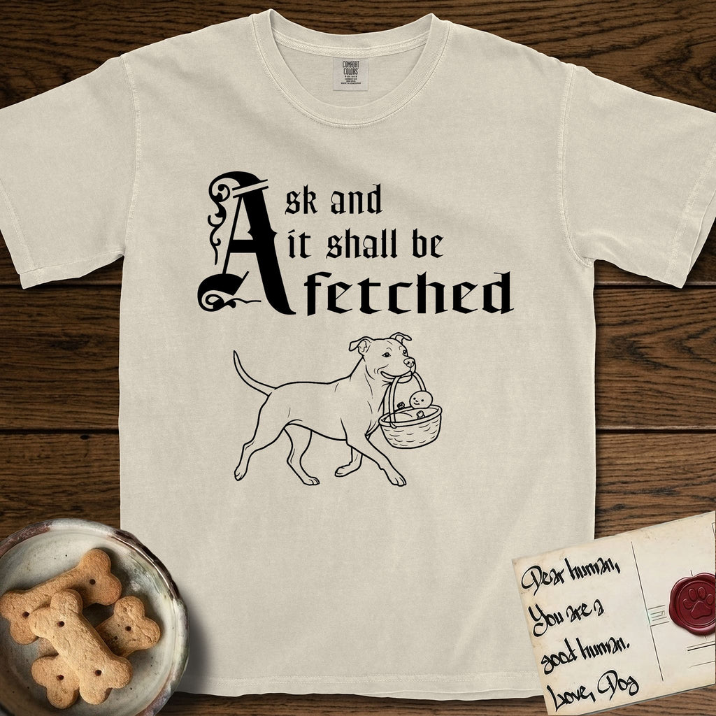 Ask and It Shall Be Fetched Pitbull T-Shirt flat lay in Ivory, featuring a sparse pen-and-ink illustration of a Pitbull at a proud trot carrying a baby in a reed basket.
