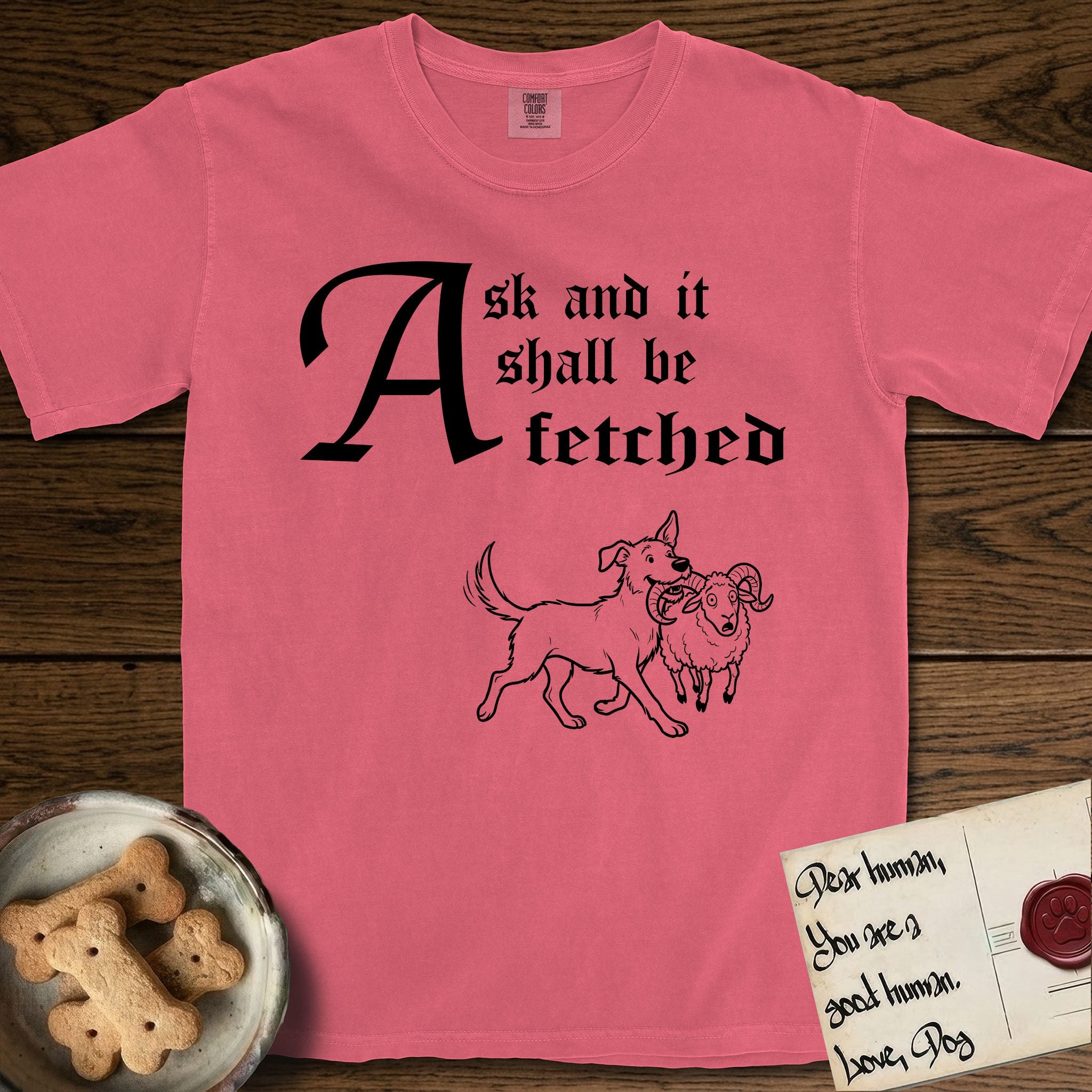 Ask and It Shall Be Fetched Rescue Mutt T-Shirt flat lay in Watermelon, featuring a sparse pen-and-ink illustration of a rescue mutt at a proud trot carrying a very surprised ram.