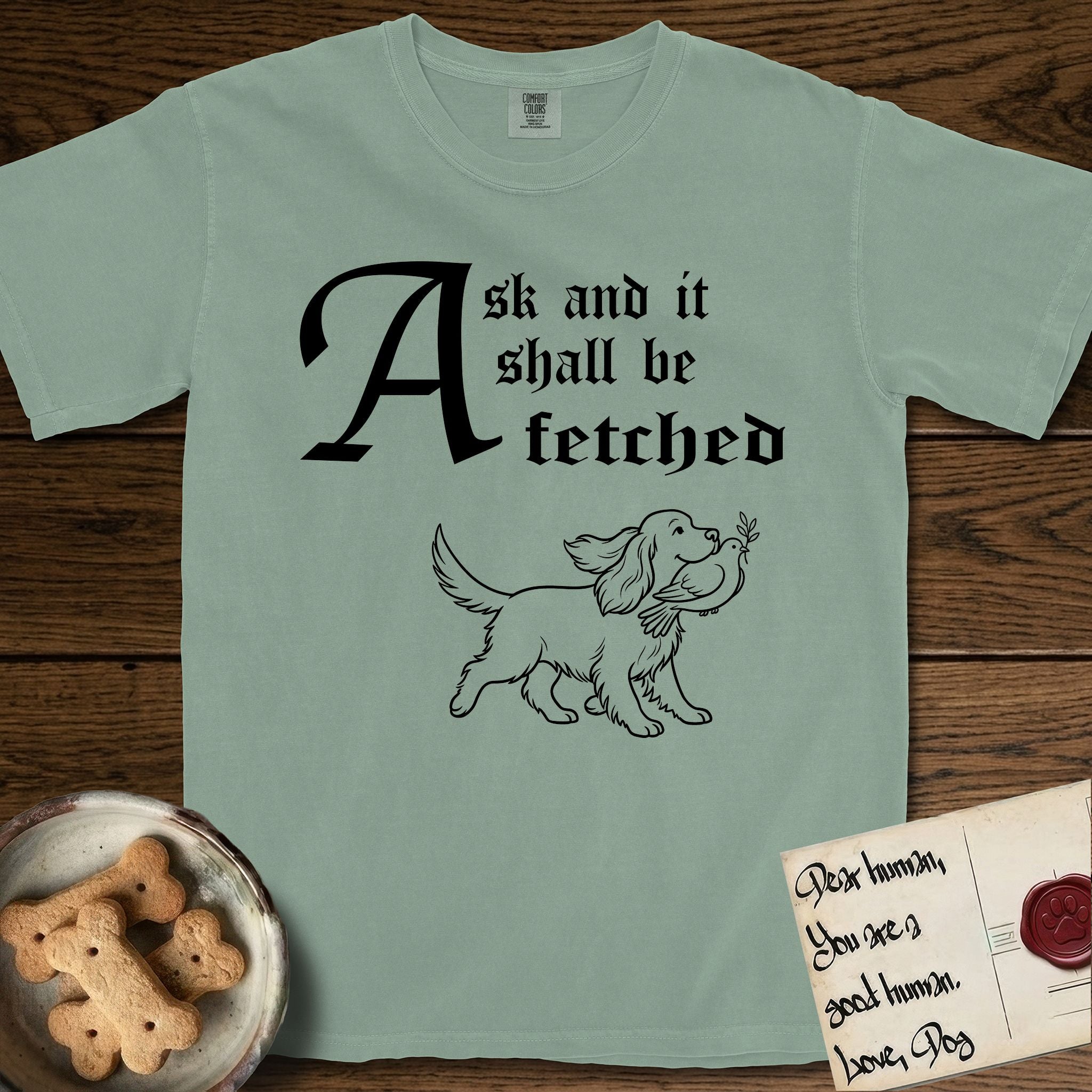 Ask and It Shall Be Fetched Spaniel T-Shirt flat lay in Bay, featuring a sparse pen-and-ink illustration of a Spaniel at a proud trot carrying a dove with an olive branch.