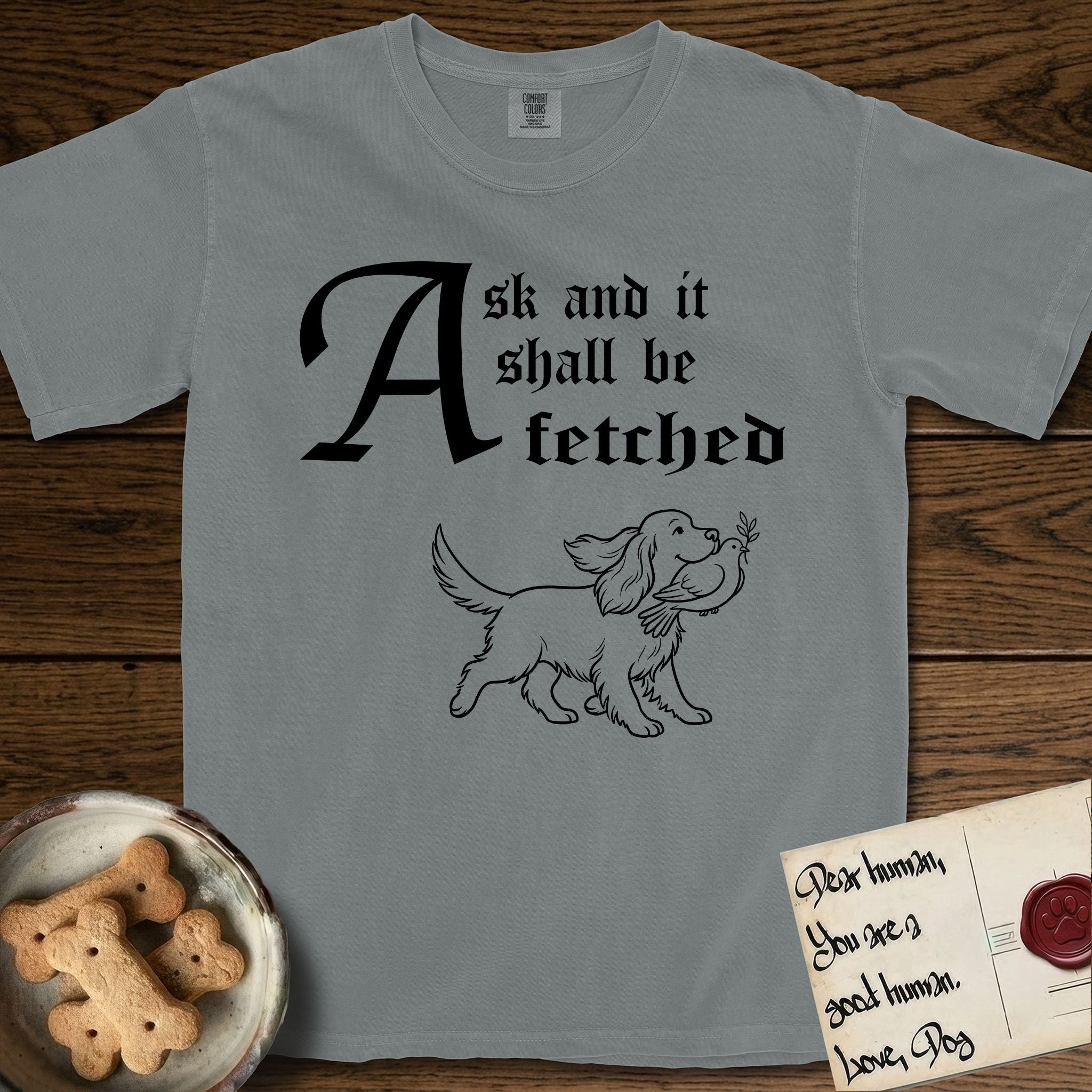 Ask and It Shall Be Fetched Spaniel T-Shirt flat lay in Granite, featuring a sparse pen-and-ink illustration of a Spaniel at a proud trot carrying a dove with an olive branch.