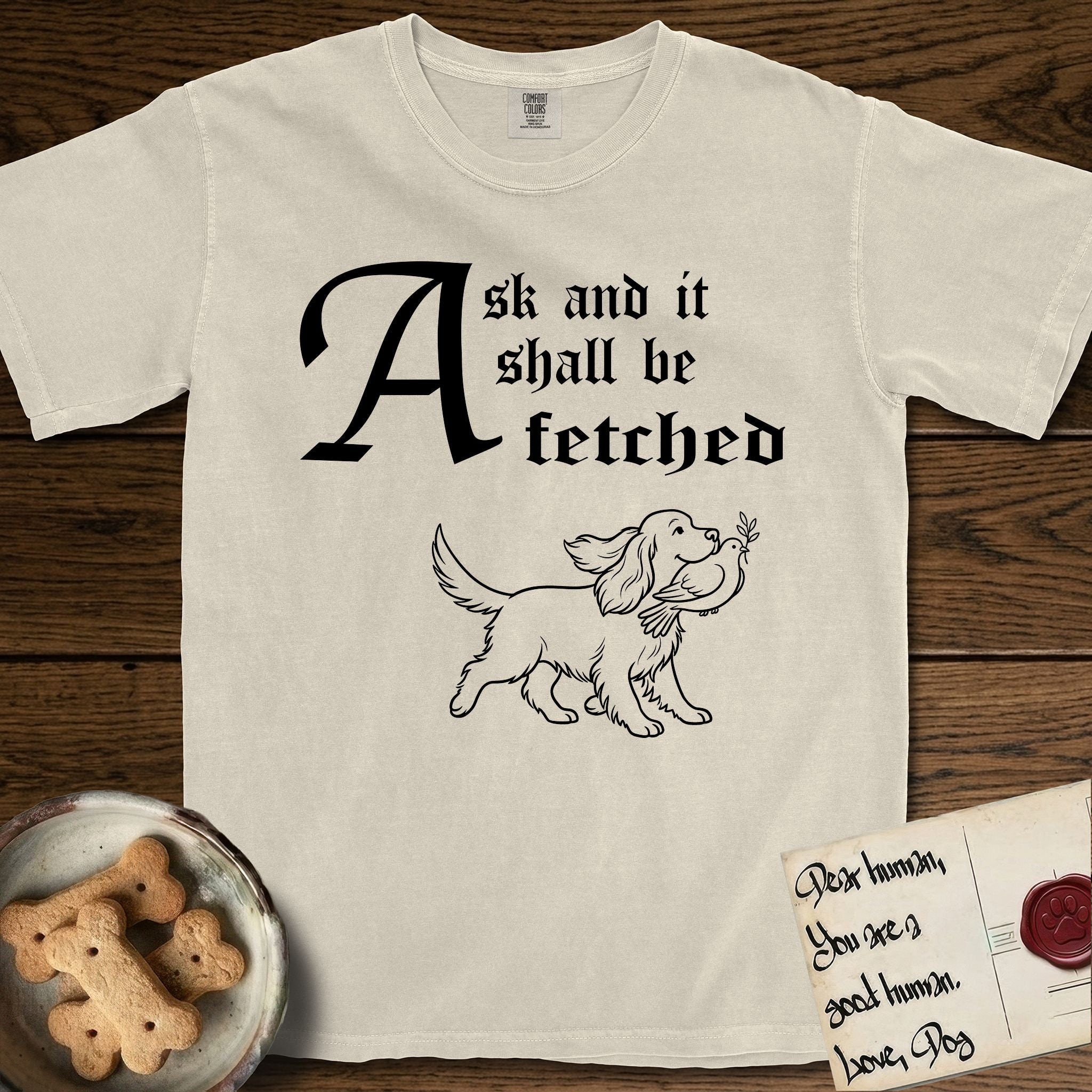 Ask and It Shall Be Fetched Spaniel T-Shirt flat lay in Ivory, featuring a sparse pen-and-ink illustration of a Spaniel at a proud trot carrying a dove with an olive branch.