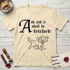 Ask and It Shall Be Fetched Spaniel T-Shirt flat lay in Natural, featuring a sparse pen-and-ink illustration of a Spaniel at a proud trot carrying a dove with an olive branch.