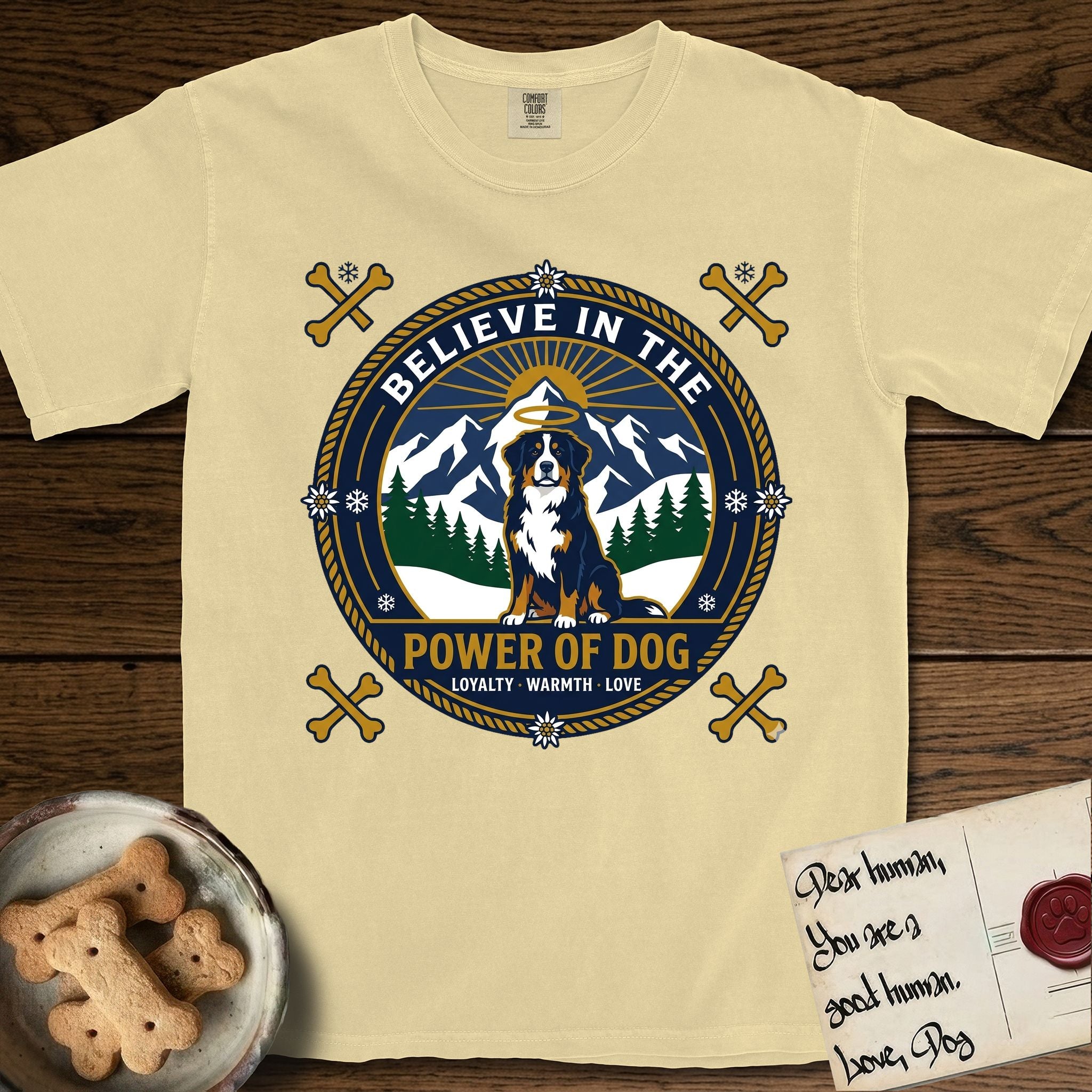 Believe in the Power of Dog Bernese Mountain Dog T-Shirt flat lay in Butter, featuring a circular national-park-style badge with a haloed Bernese Mountain Dog, a mountain scene, a rope border, and the words Loyalty, Warmth, Love.