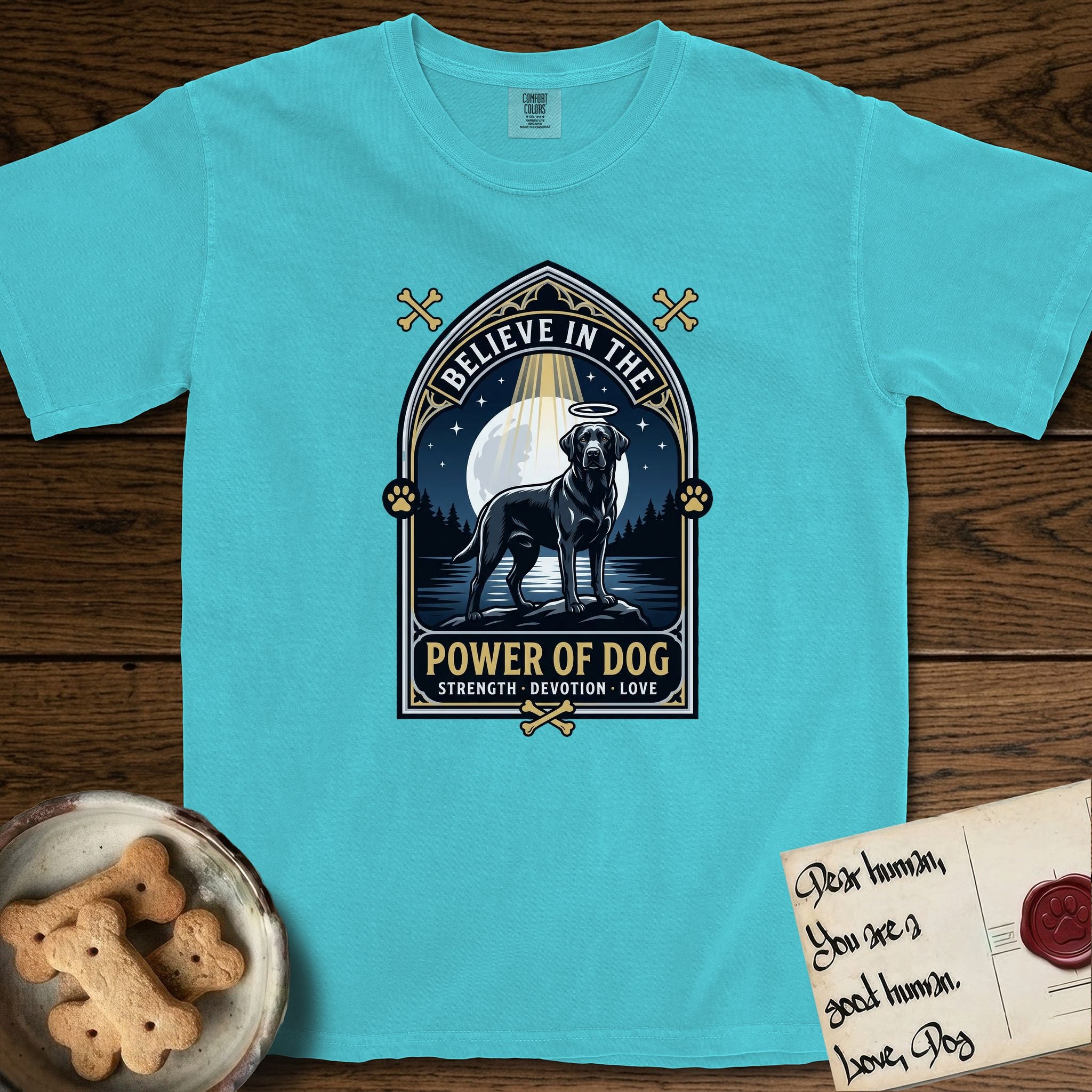 Believe in the Power of Dog Black Lab T-Shirt flat lay in Lagoon Blue, featuring a dramatic gothic-arch badge with a moonlit Black Lab on a rock above still water, a beam of light through the arch, and the words Strength, Devotion, Love.