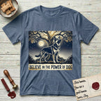 Believe in the Power of Dog German Shepherd T-Shirt flat lay in Heather Indigo, featuring a moonlit illustration of a German Shepherd standing beneath a great tree whose roots and branches reach equally in both directions.