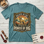 Believe in the Power of Dog Golden Retriever T-Shirt flat lay in Heather Galapagos Blue, featuring a vintage outdoor badge with a haloed Golden Retriever standing on a rock above the treeline at sunrise and the words Faith, Loyalty, Love.