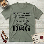Believe in the Power of Dog Labrador T-Shirt flat lay in Sage, featuring stark minimalist single-line art of a Labrador with bold stacked "Believe in the Power of Dog" type and a paw-print heart in the O.