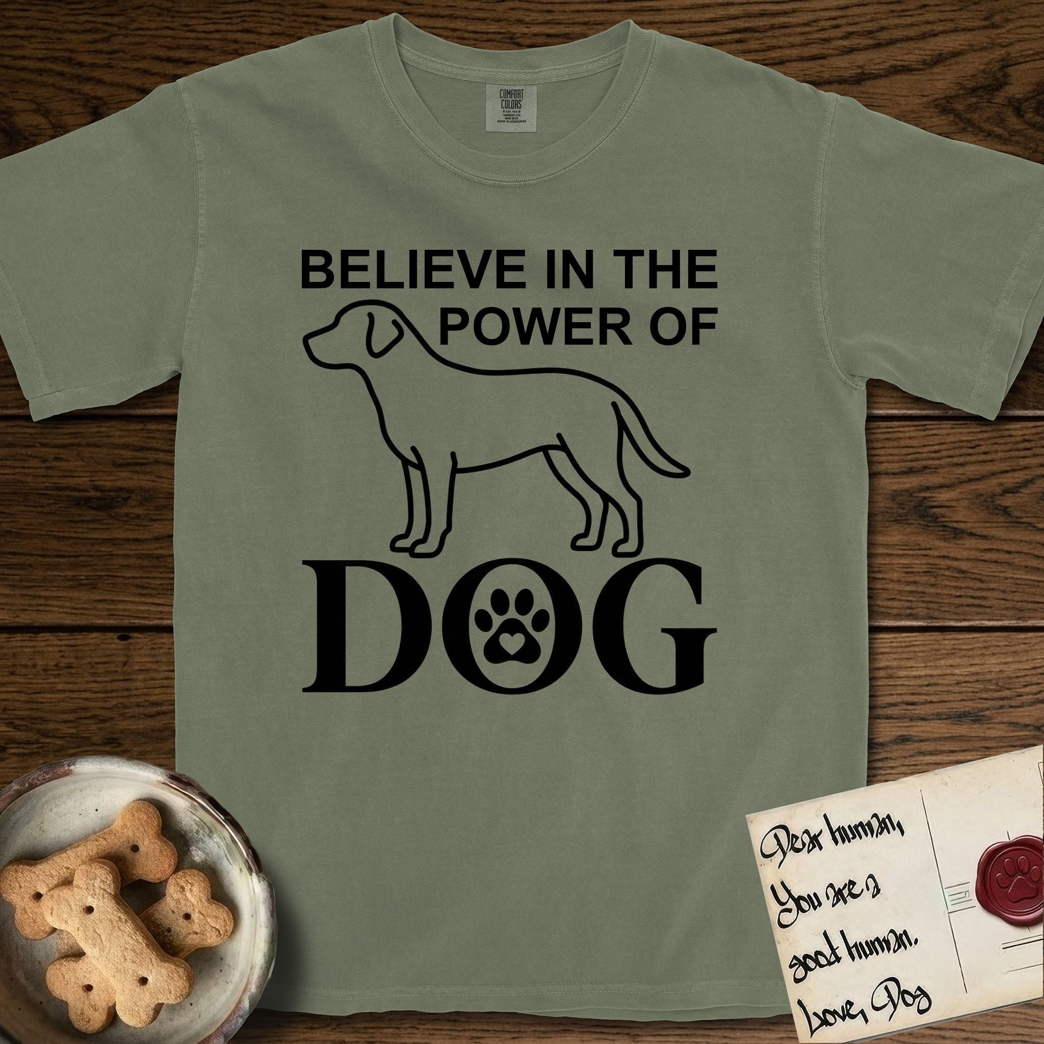 Believe in the Power of Dog Labrador T-Shirt flat lay in Sage, featuring stark minimalist single-line art of a Labrador with bold stacked "Believe in the Power of Dog" type and a paw-print heart in the O.
