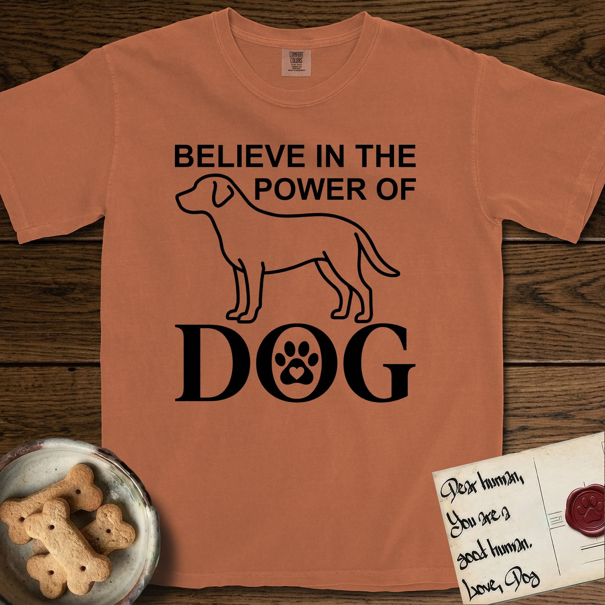 Believe in the Power of Dog Labrador T-Shirt flat lay in Yam, featuring stark minimalist single-line art of a Labrador with bold stacked "Believe in the Power of Dog" type and a paw-print heart in the O.