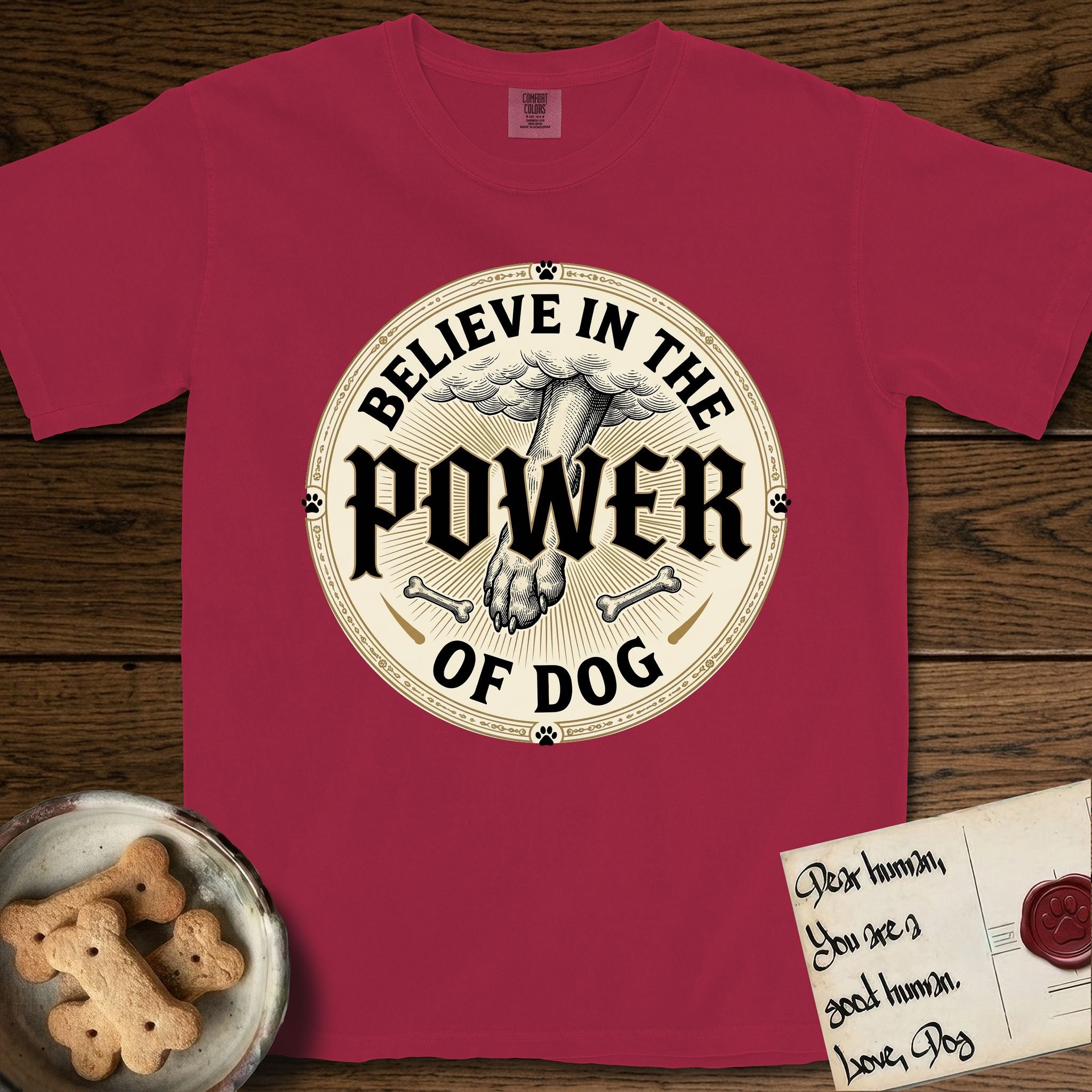 Believe in the Power of Dog Paw T-Shirt flat lay in Chili, featuring a vintage engraving medallion of a Dog paw and a human hand meeting over crossed bones in a sunburst.