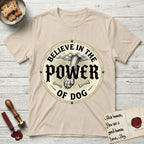 Believe in the Power of Dog Paw T-Shirt flat lay in Sand, featuring a vintage engraving medallion of a Dog paw and a human hand meeting over crossed bones in a sunburst.