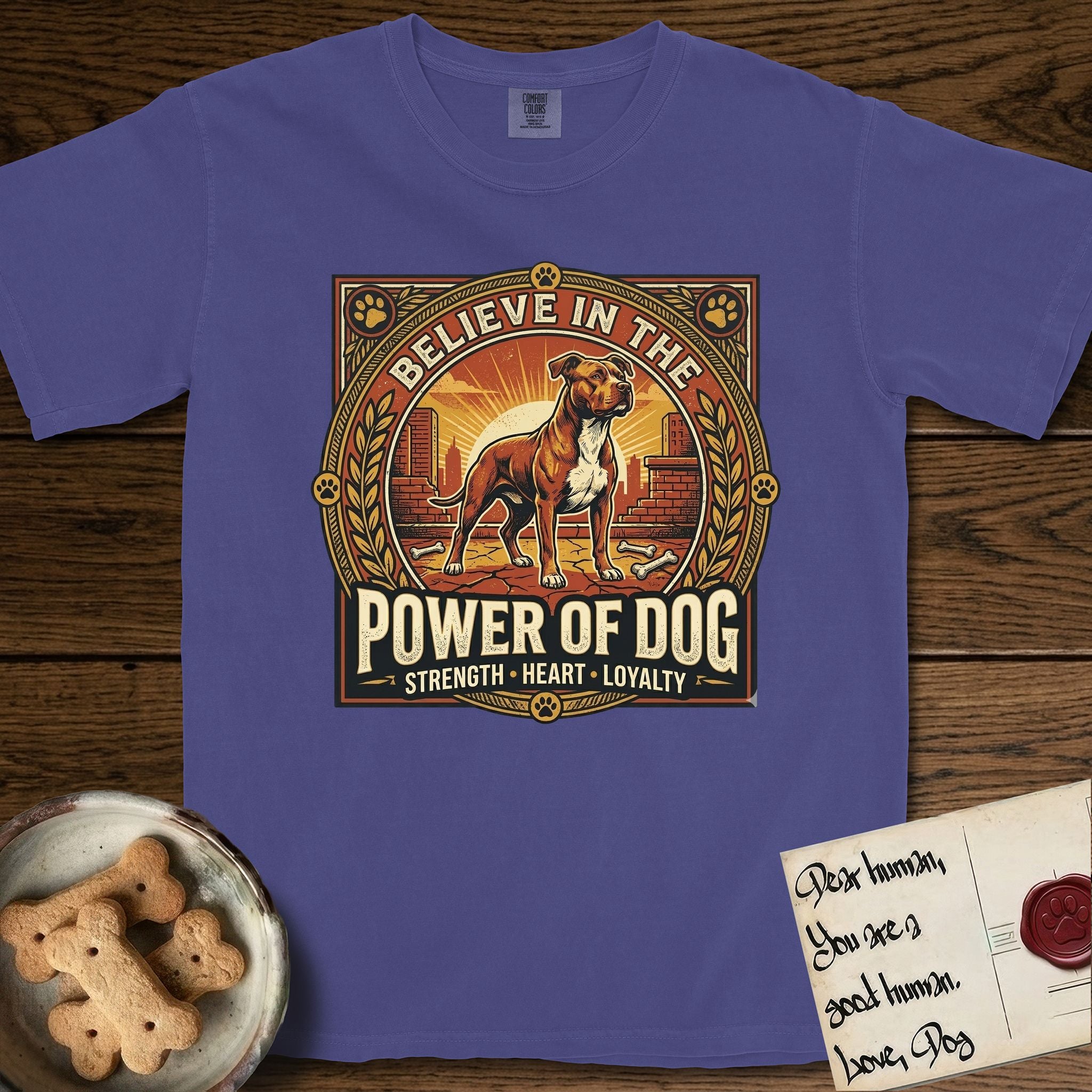 Believe in the Power of Dog Pitbull T-Shirt flat lay in Grape, featuring a vintage urban badge with a brick-red Pitbull, a city skyline, a radiating sun, and the words Strength, Heart, Loyalty.