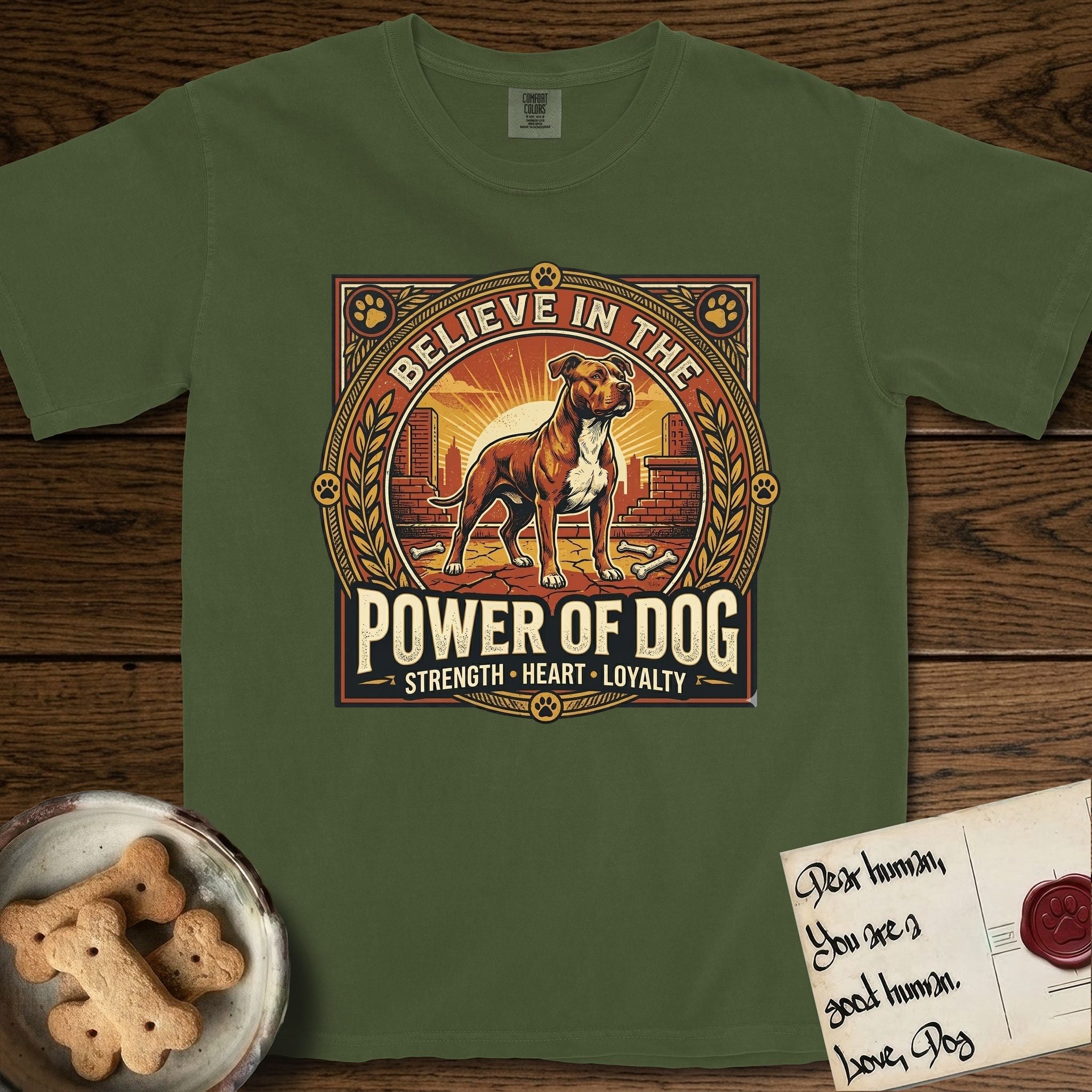 Believe in the Power of Dog Pitbull T-Shirt flat lay in Hemp, featuring a vintage urban badge with a brick-red Pitbull, a city skyline, a radiating sun, and the words Strength, Heart, Loyalty.
