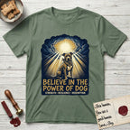 Believe in the Power of Dog Pitbull Clouds T-Shirt flat lay in Military Green, featuring a devotional badge with a seated Pitbull, parting clouds and radiating light, and the words Strength, Resilience, Redemption.