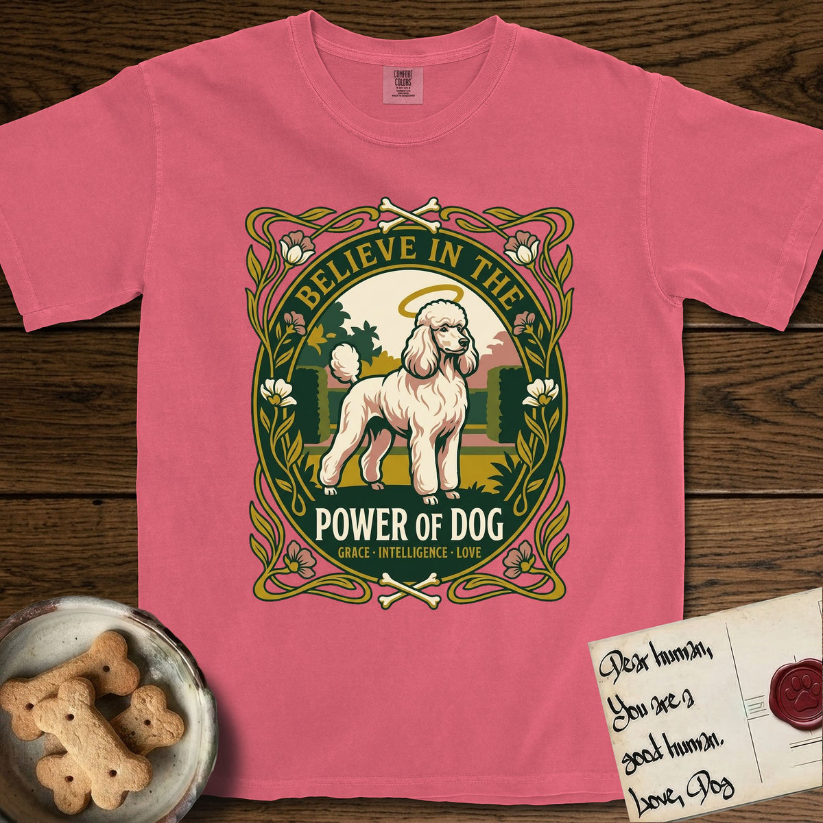 Believe in the Power of Dog Poodle T-Shirt flat lay in Watermelon, featuring an Art Nouveau floral badge with a haloed Poodle in a garden park scene and the words Grace, Intelligence, Love.