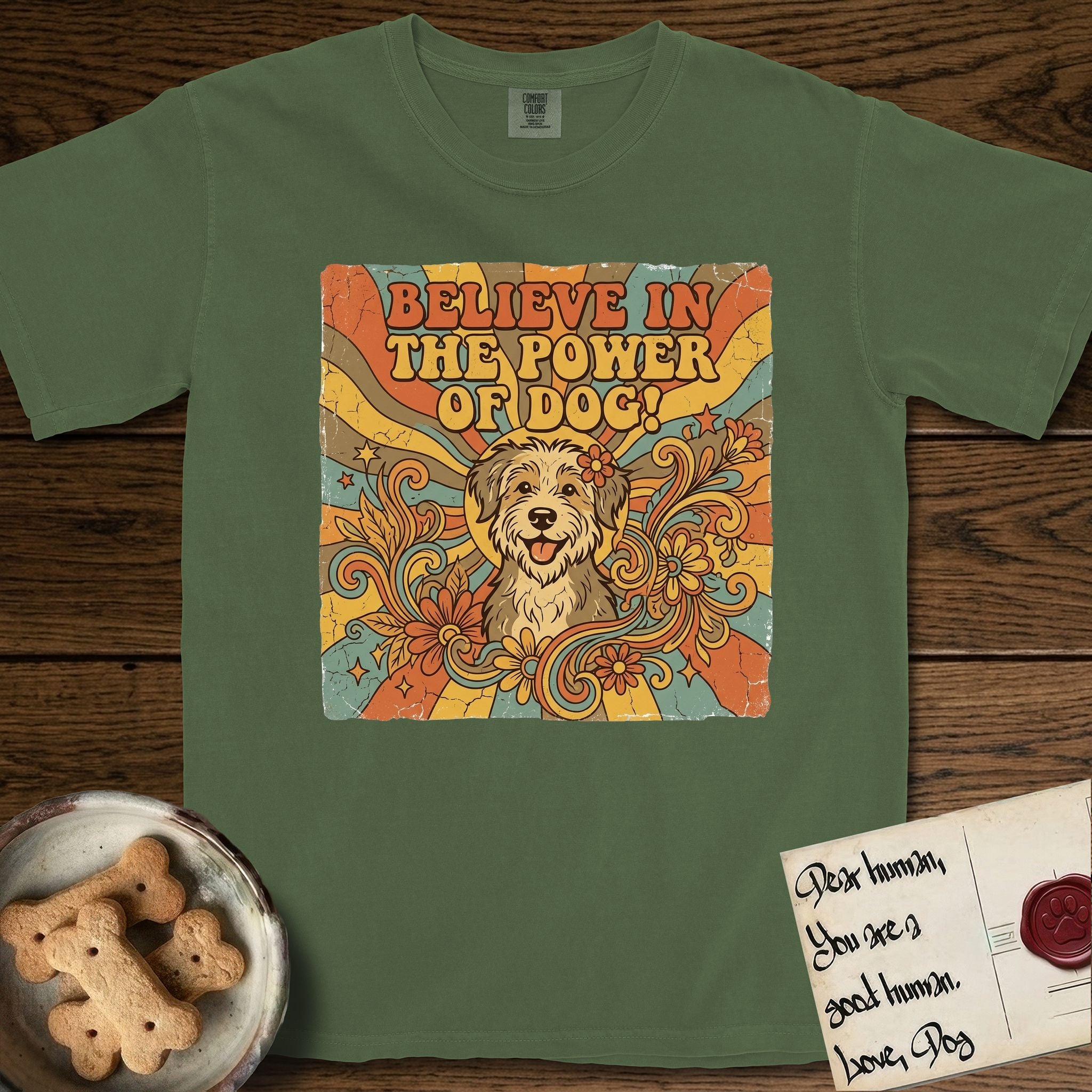 Believe in the Power of Dog Rescue Mutt T-Shirt flat lay in Moss, featuring a retro 1970s groovy poster of a grinning rescue mutt with a radiating sunburst and swirling florals.