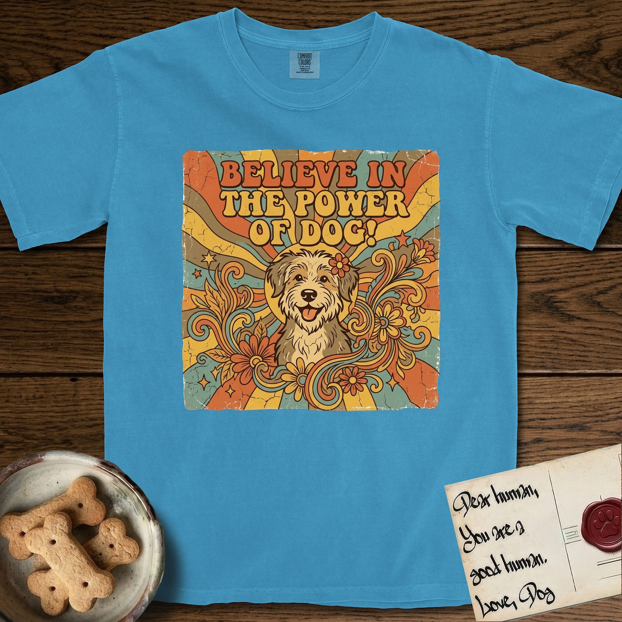 Believe in the Power of Dog Rescue Mutt T-Shirt flat lay in Royal Caribe, featuring a retro 1970s groovy poster of a grinning rescue mutt with a radiating sunburst and swirling florals.