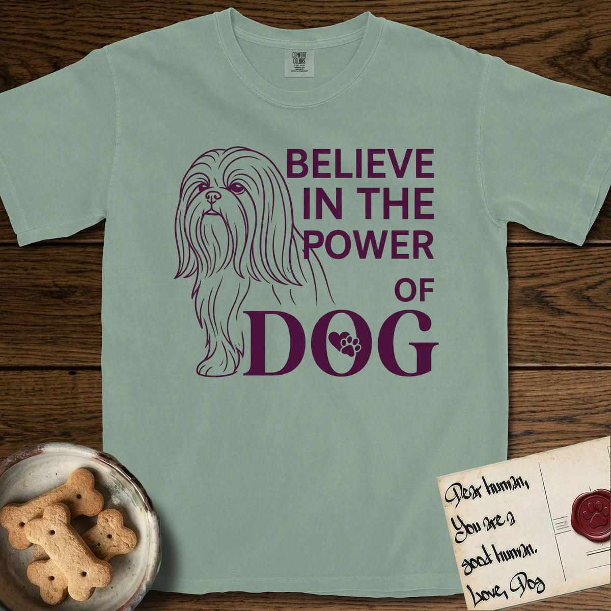 Believe in the Power of Dog Shih Tzu T-Shirt flat lay in Bay, featuring a clean single-color line drawing of a long-coated Shih Tzu beside the stacked words Believe in the Power of Dog with a paw print pressed into the O.