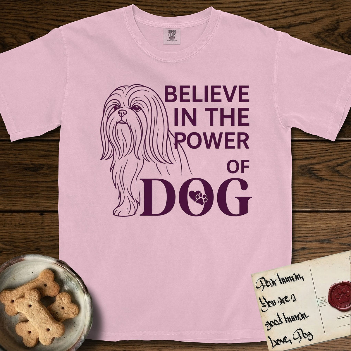 Believe in the Power of Dog Shih Tzu T-Shirt flat lay in Blossom, featuring a clean single-color line drawing of a long-coated Shih Tzu beside the stacked words Believe in the Power of Dog with a paw print pressed into the O.