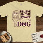 Believe in the Power of Dog Shih Tzu T-Shirt flat lay in Butter, featuring a clean single-color line drawing of a long-coated Shih Tzu beside the stacked words Believe in the Power of Dog with a paw print pressed into the O.