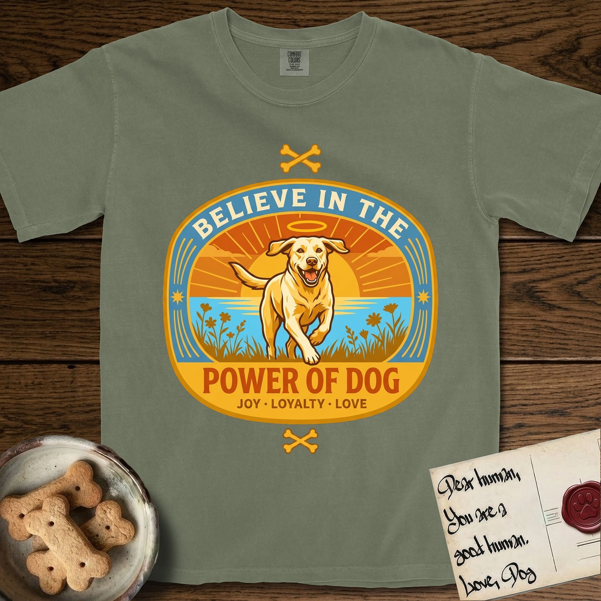 Believe in the Power of Dog Yellow Lab T-Shirt flat lay in Sage, featuring a vintage oval badge with a haloed Yellow Lab running through a field of wildflowers and the words Joy, Loyalty, Love.