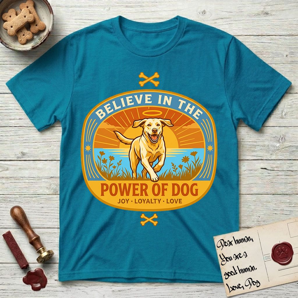 Believe in the Power of Dog Yellow Lab T-Shirt flat lay in Tropical Blue, featuring a vintage oval badge with a haloed Yellow Lab running through a field of wildflowers and the words Joy, Loyalty, Love.