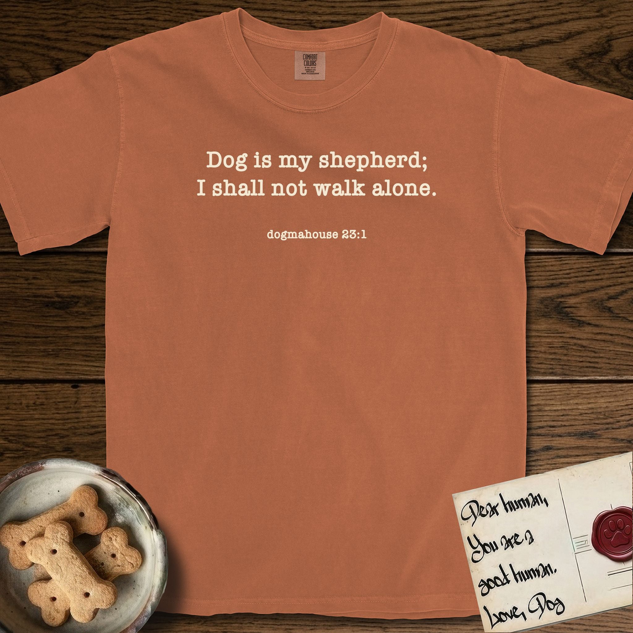 Dog is My Shepherd T-Shirt flat lay in Yam, featuring Small centered typewriter-type text reading Dog is my shepherd; I shall not walk alone, with the citation dogmahouse 23:1 beneath it.