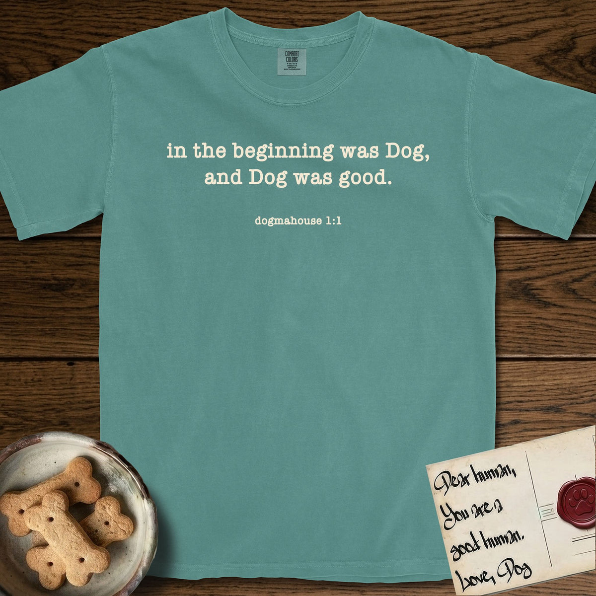 In the Beginning T-Shirt flat lay in Blue Spruce, featuring Small centered typewriter-type text reading in the beginning was Dog, and Dog was good, with the citation dogmahouse 1:1 beneath it.
