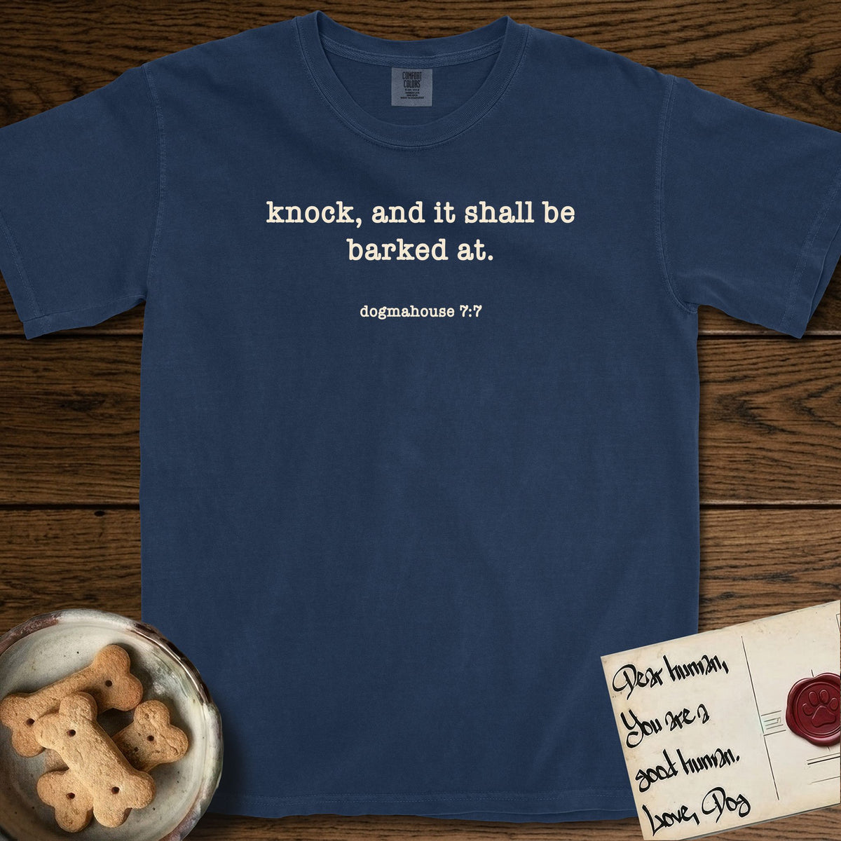 Knock T-Shirt flat lay in True Navy, featuring Small centered typewriter-type text reading knock, and it shall be barked at, with the citation dogmahouse 7:7 beneath it.