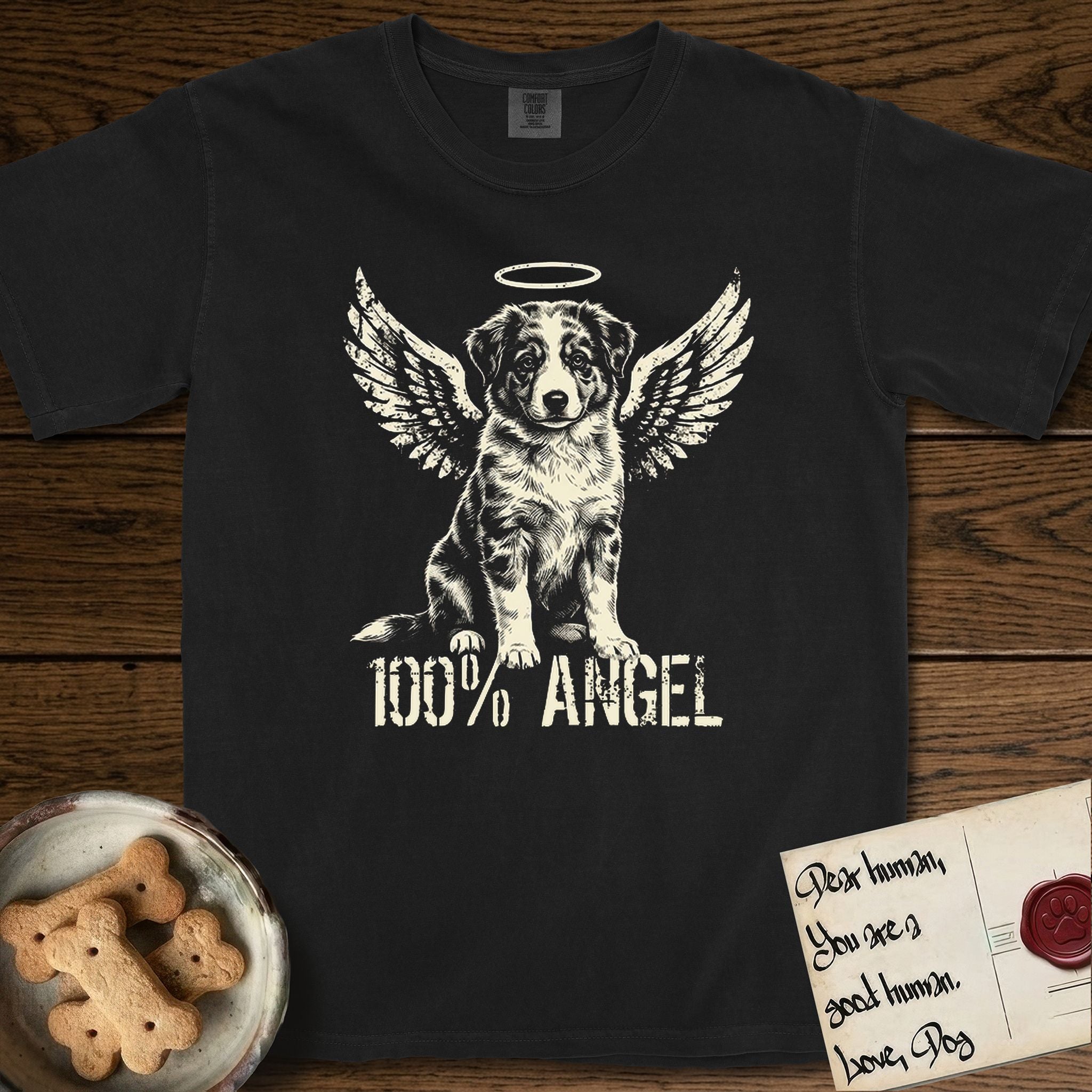 Australian Shepherd T-Shirt flat lay in Black, featuring Distressed cream one-color screen-print of a blue merle Australian Shepherd puppy as an angel, wings raised and a halo above, with 100% ANGEL lettering across the bottom.