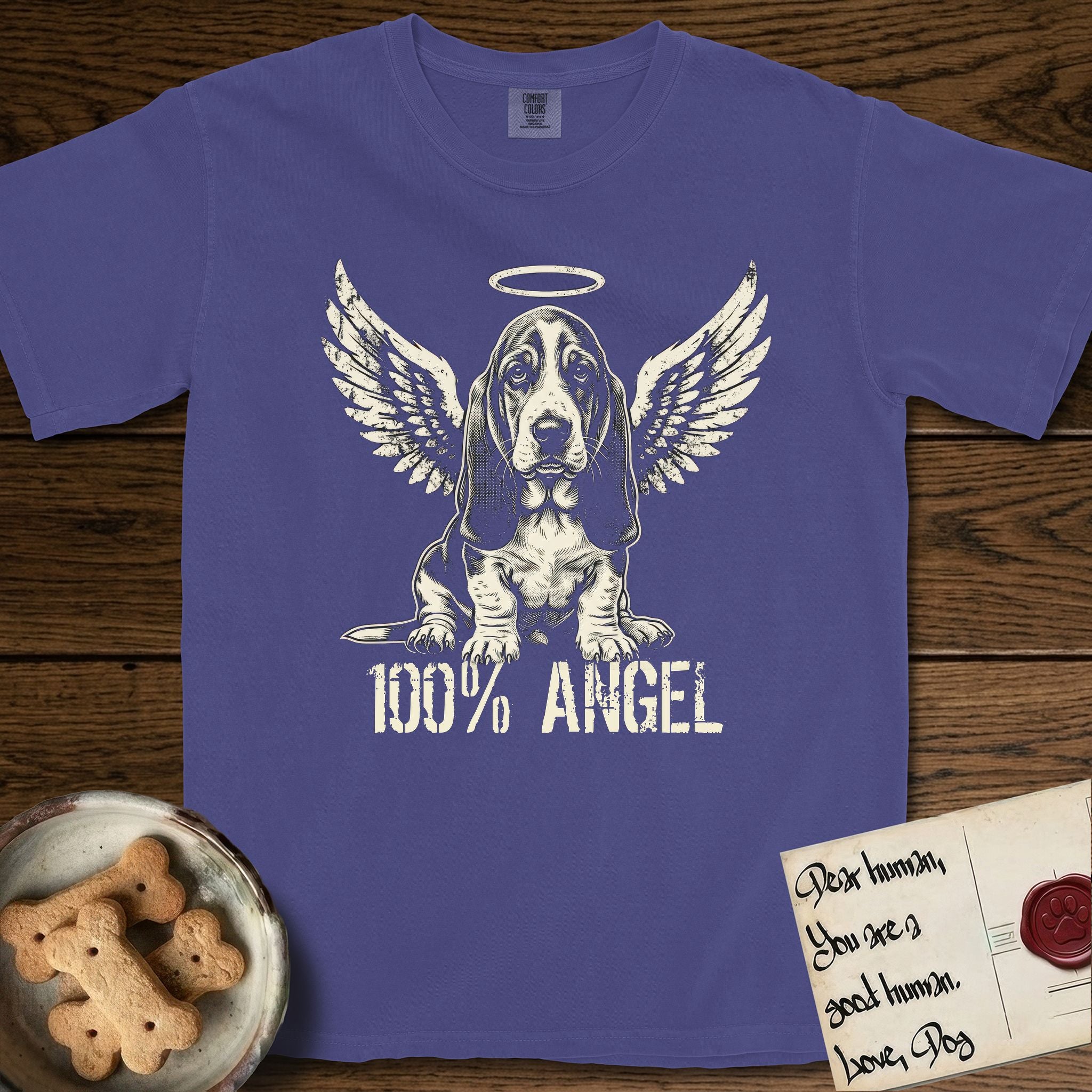 Basset Hound T-Shirt flat lay in Grape, featuring Distressed cream one-color screen-print of a Basset Hound puppy as an angel, long ears draping forward, wings spread and a halo above, with 100% ANGEL lettering across the bottom.