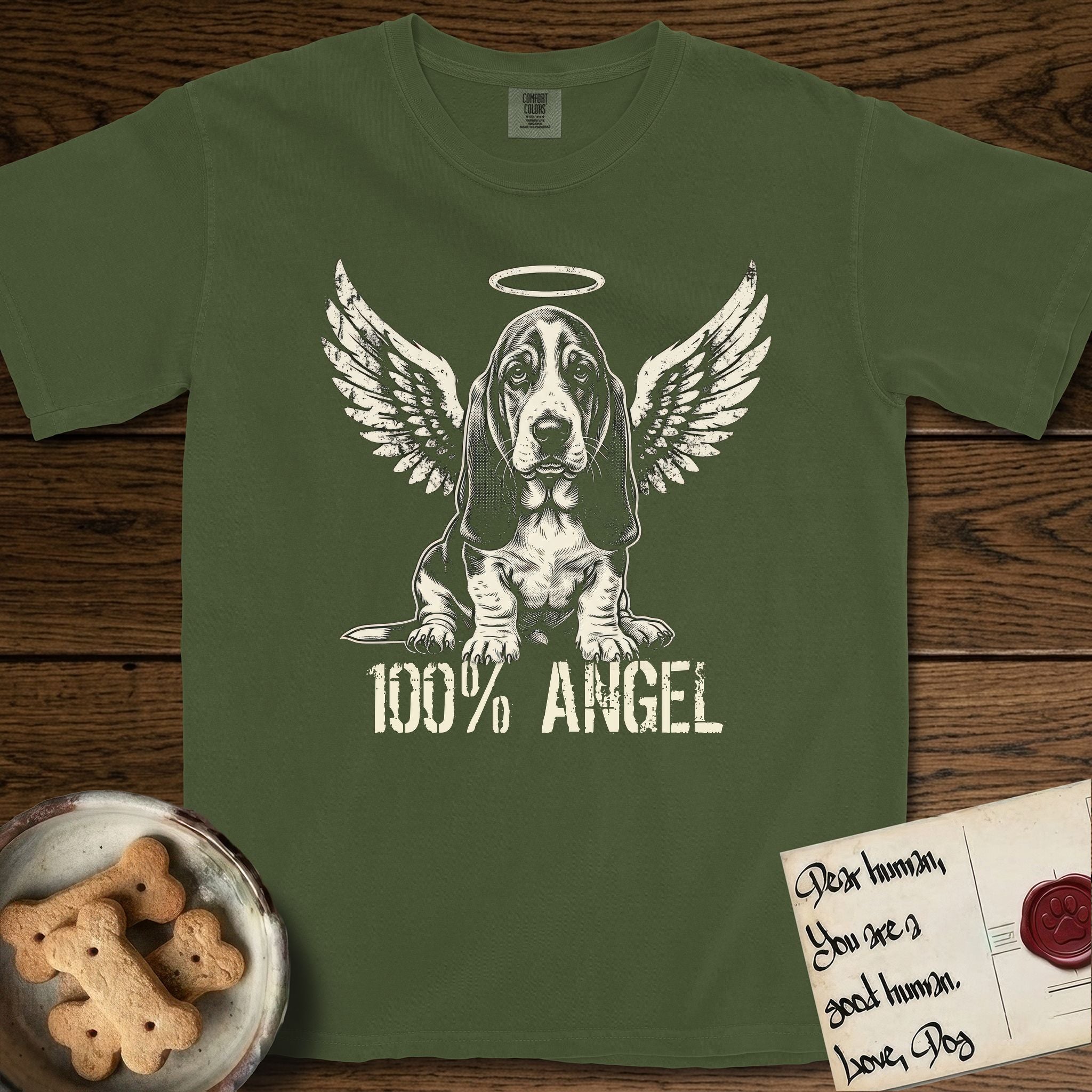 Basset Hound T-Shirt flat lay in Hemp, featuring Distressed cream one-color screen-print of a Basset Hound puppy as an angel, long ears draping forward, wings spread and a halo above, with 100% ANGEL lettering across the bottom.