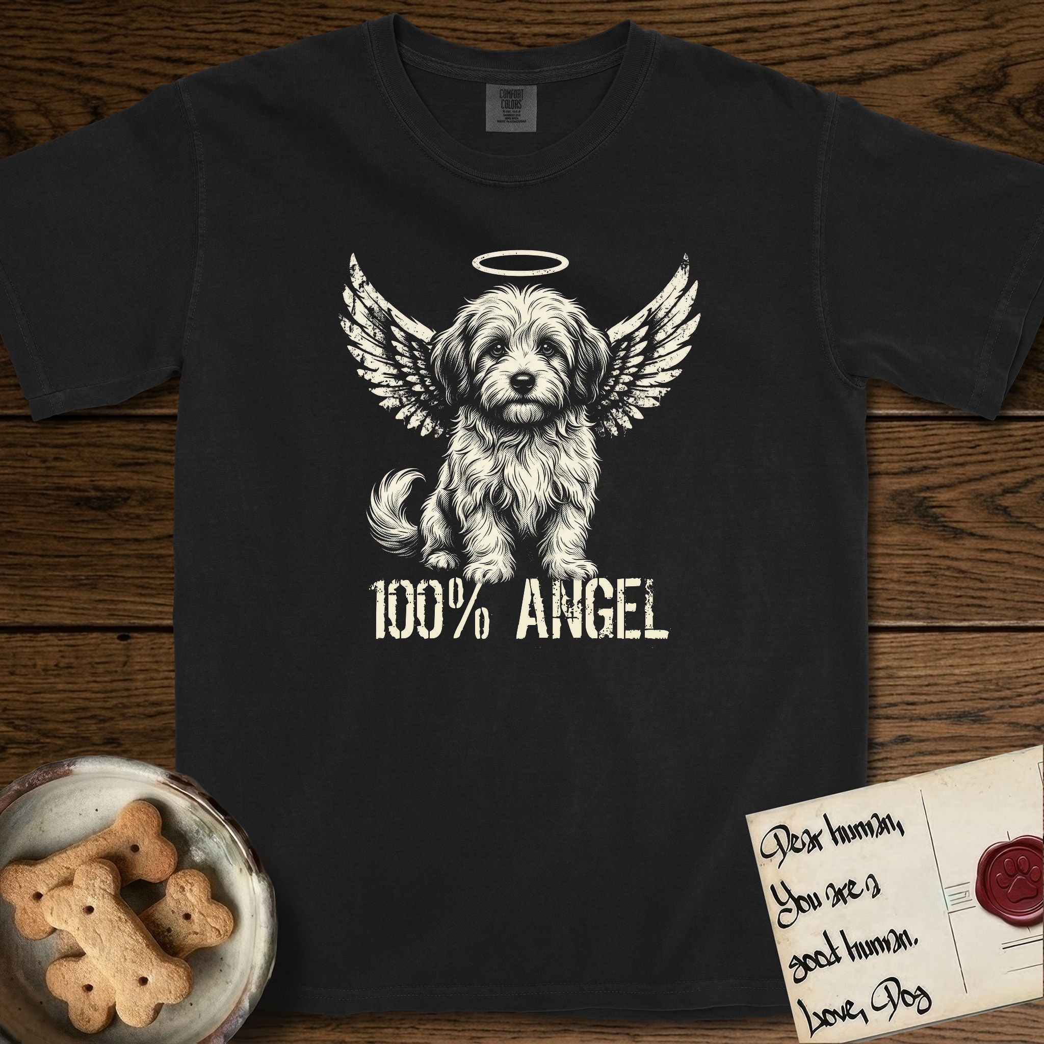 Coton de Tulear T-Shirt flat lay in Black, featuring Distressed cream one-color screen-print of a fluffy white Coton de Tulear puppy as an angel, plumed tail curled beside him, wings spread and a halo above, with 100% ANGEL lettering across the bottom.