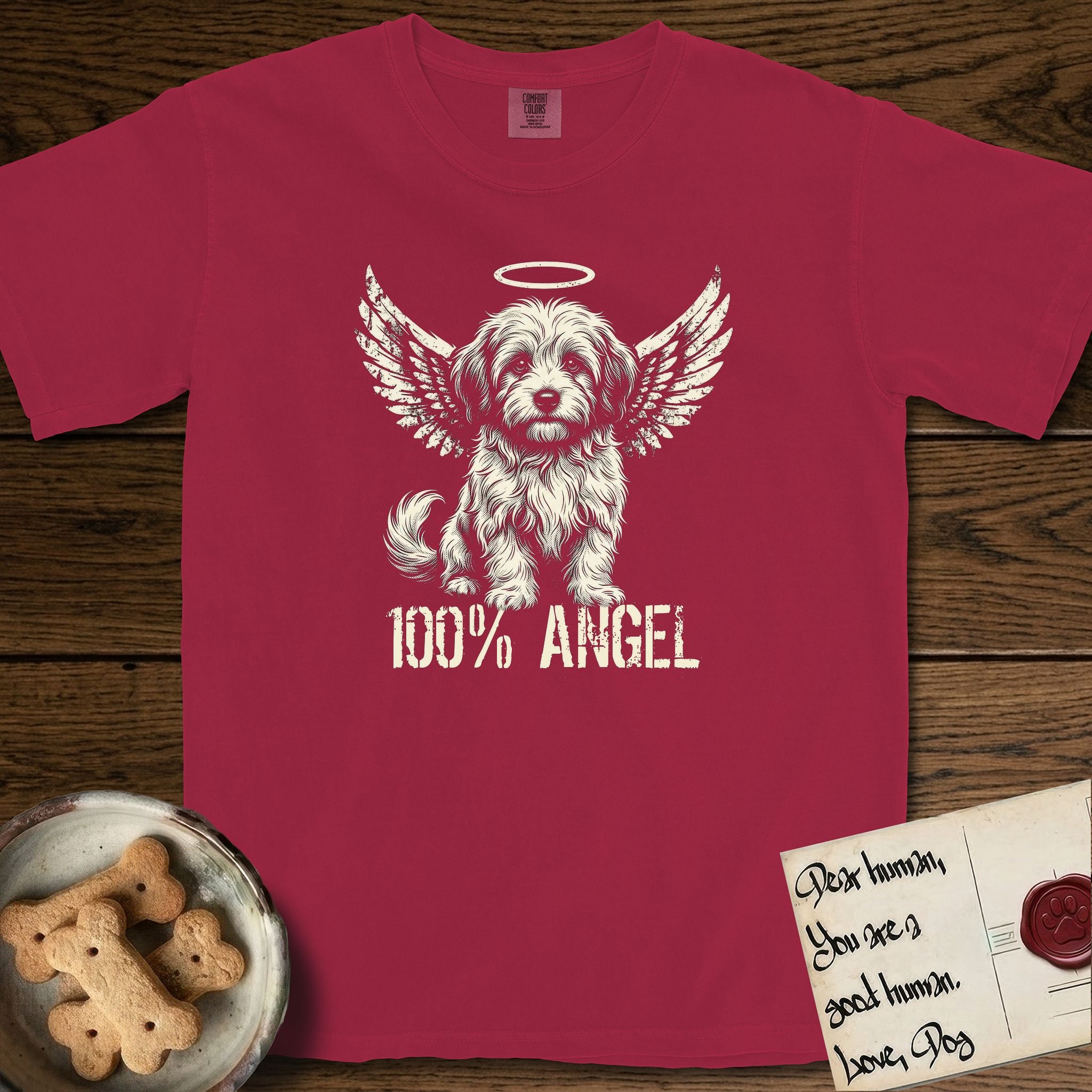 Coton de Tulear T-Shirt flat lay in Chili, featuring Distressed cream one-color screen-print of a fluffy white Coton de Tulear puppy as an angel, plumed tail curled beside him, wings spread and a halo above, with 100% ANGEL lettering across the bottom.