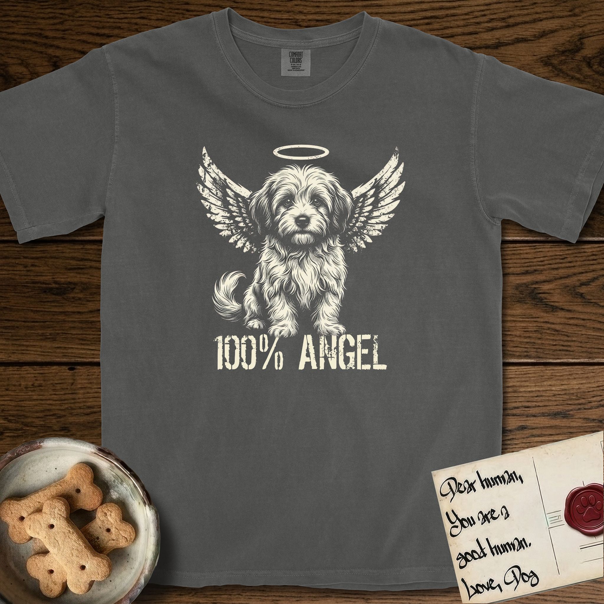 Coton de Tulear T-Shirt flat lay in Pepper, featuring Distressed cream one-color screen-print of a fluffy white Coton de Tulear puppy as an angel, plumed tail curled beside him, wings spread and a halo above, with 100% ANGEL lettering across the bottom.
