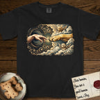 Creation of Adam T-Shirt flat lay in Black, featuring a baroque ornamental frame with a Golden Retriever emerging from clouds extending a paw toward a reaching human hand, a small angel beside them, and a glowing point of contact.