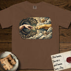 Creation of Adam T-Shirt flat lay in Espresso, featuring a baroque ornamental frame with a Golden Retriever emerging from clouds extending a paw toward a reaching human hand, a small angel beside them, and a glowing point of contact.