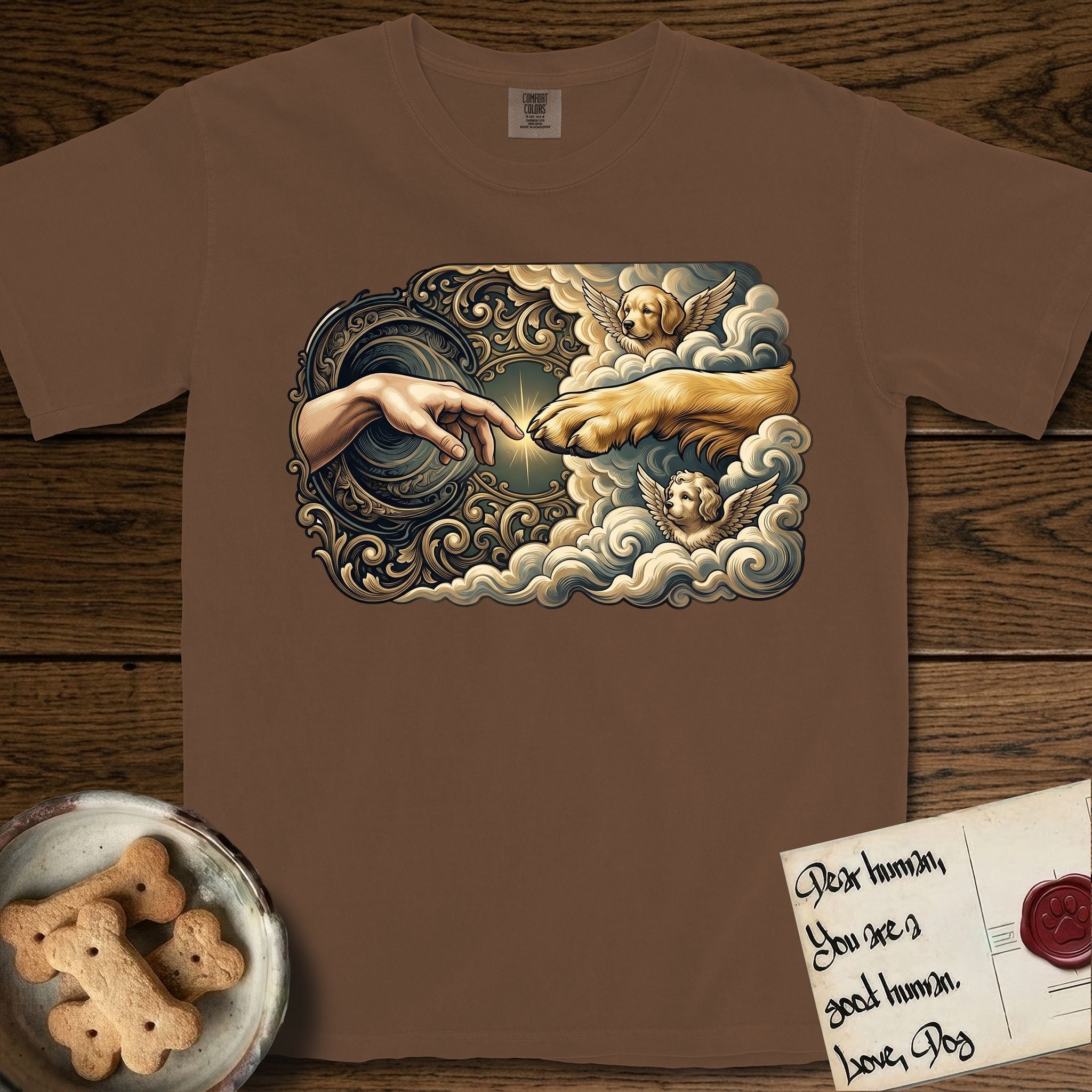 Creation of Adam T-Shirt flat lay in Espresso, featuring a baroque ornamental frame with a Golden Retriever emerging from clouds extending a paw toward a reaching human hand, a small angel beside them, and a glowing point of contact.