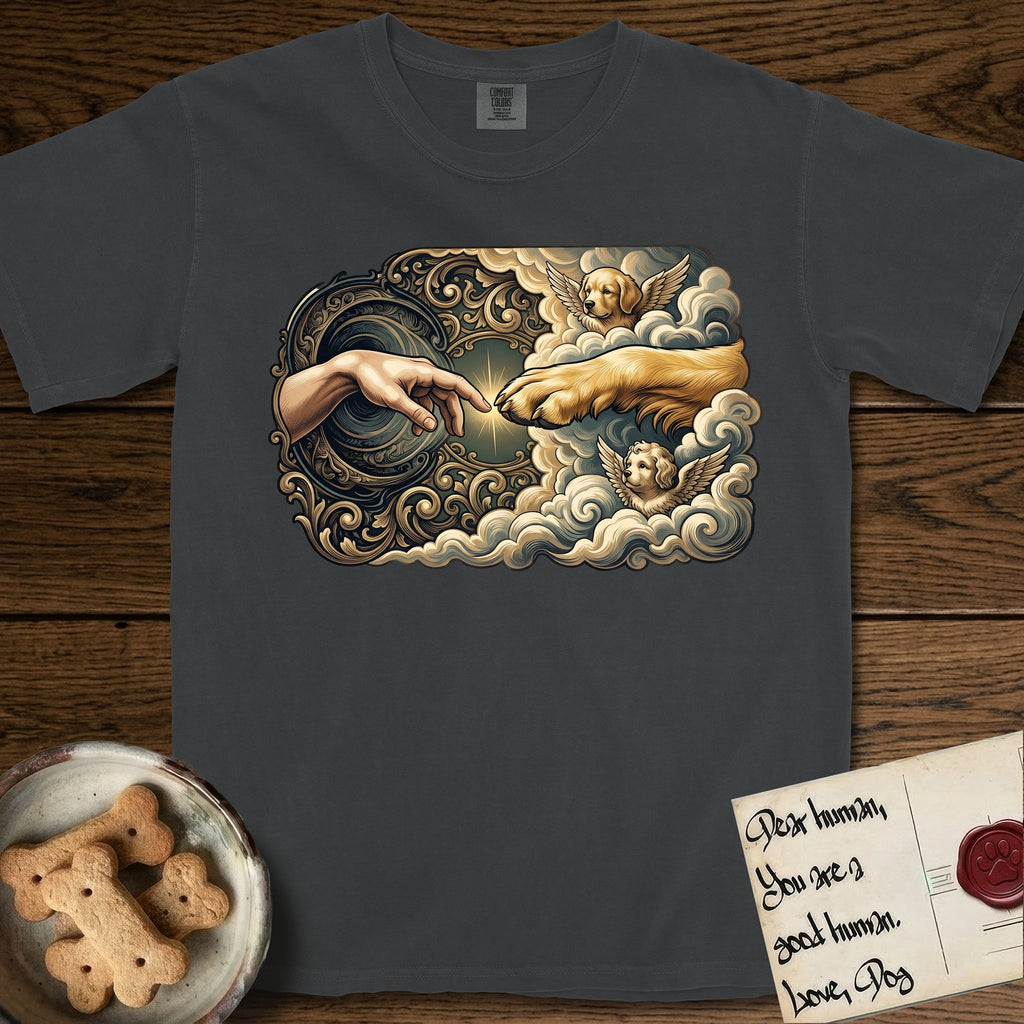 Creation of Adam T-Shirt flat lay in Graphite, featuring a baroque ornamental frame with a Golden Retriever emerging from clouds extending a paw toward a reaching human hand, a small angel beside them, and a glowing point of contact.