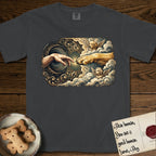 Creation of Adam T-Shirt flat lay in Graphite, featuring a baroque ornamental frame with a Golden Retriever emerging from clouds extending a paw toward a reaching human hand, a small angel beside them, and a glowing point of contact.