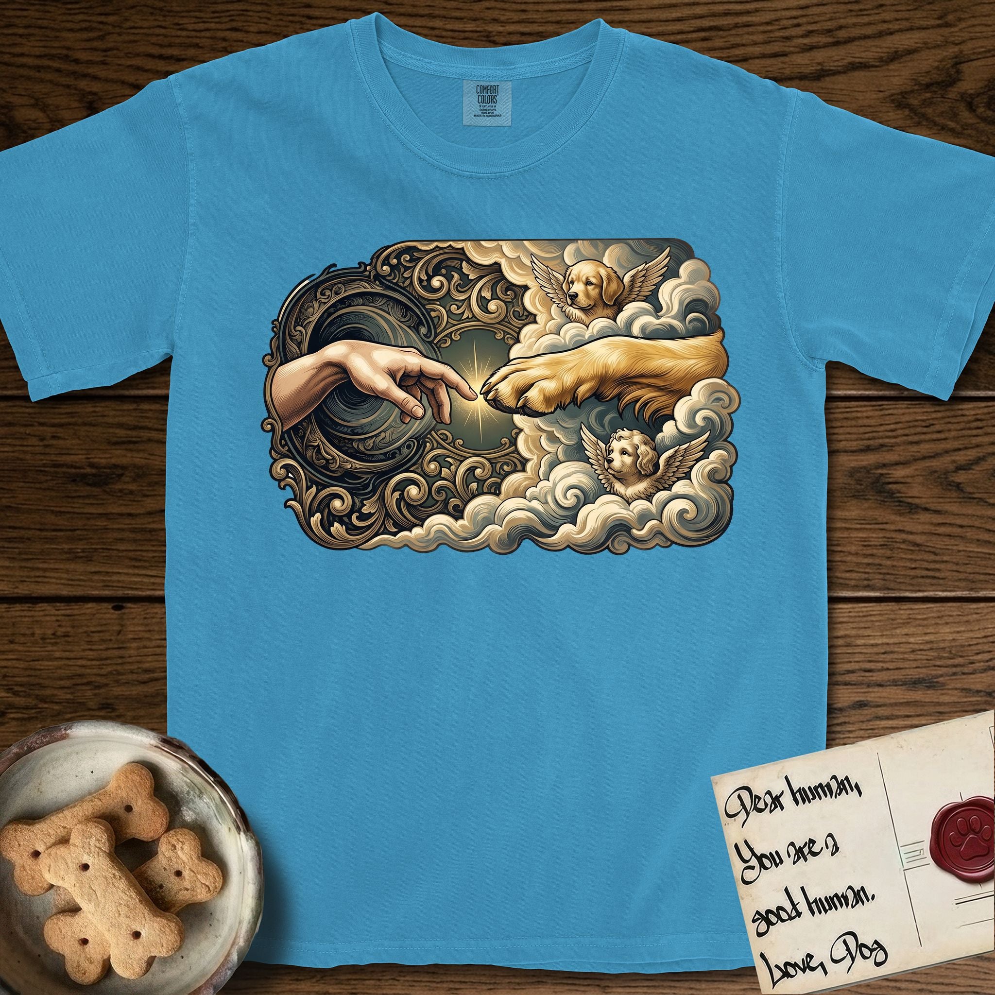 Creation of Adam T-Shirt flat lay in Royal Caribe, featuring a baroque ornamental frame with a Golden Retriever emerging from clouds extending a paw toward a reaching human hand, a small angel beside them, and a glowing point of contact.